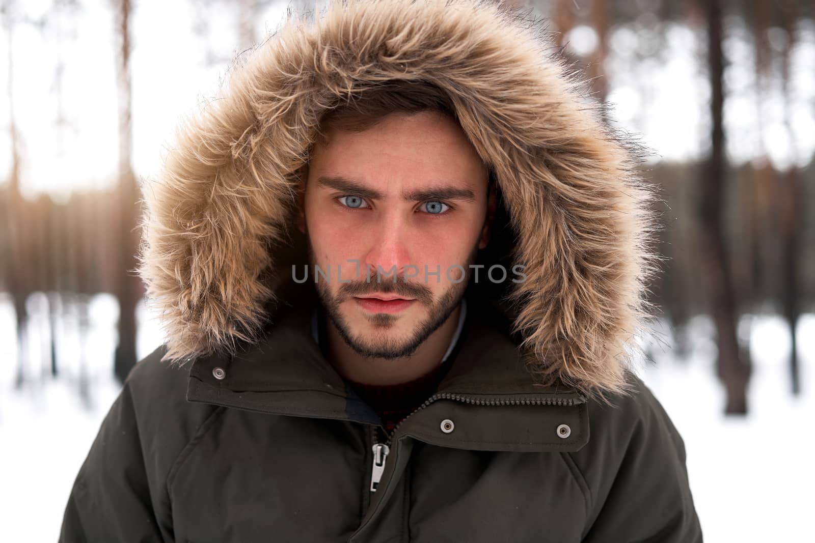 Handsome serious brutal bearded young caucasian man standing outdoors fur hood in winter season forest. Attractive stylish european guy walking snowy christmas woodland Season holiday leisure