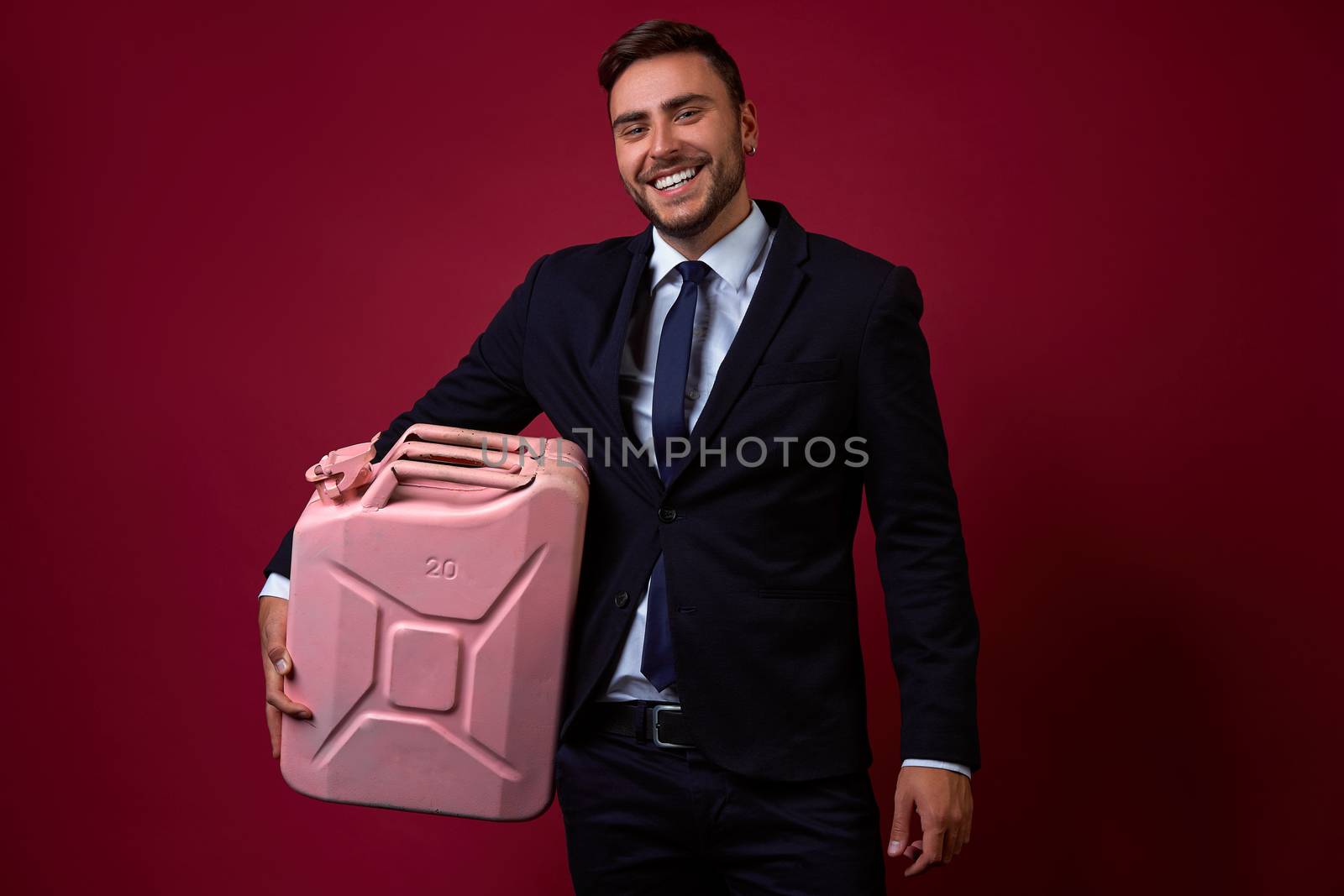 Portrait young smiling businessman. Caucasian guy business suit studio red background. Modern business person Holding canister gasoline in his hands. Portrait of charming successful happy entrepreneur