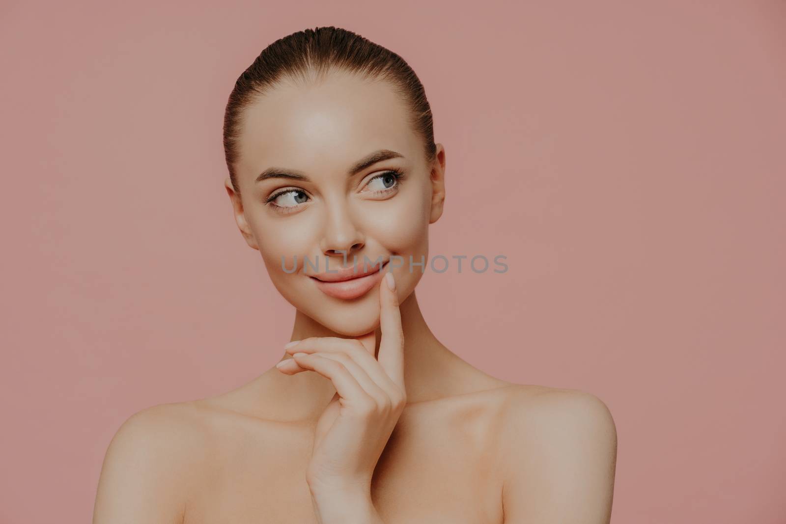 Topless thoughtful lady with clean perfect skin, dark hair, looks aside, undergoes facial trearrments, poses indoor, isolated over rosy background. Cosmetology, skin care and wellness concept by vkstock