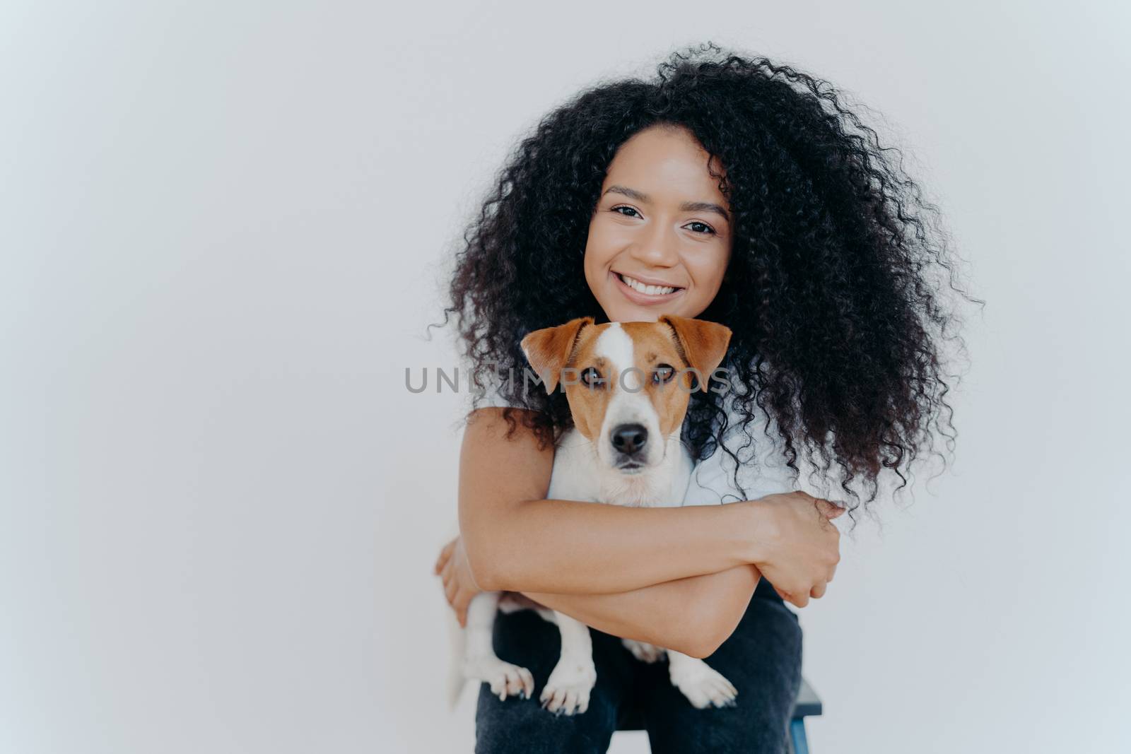 People, animal or pet care concept. Curly haired woman embraces favourite dog, smiles pleasantly, stands against white background, copy space area for your advertising content. Good friends.