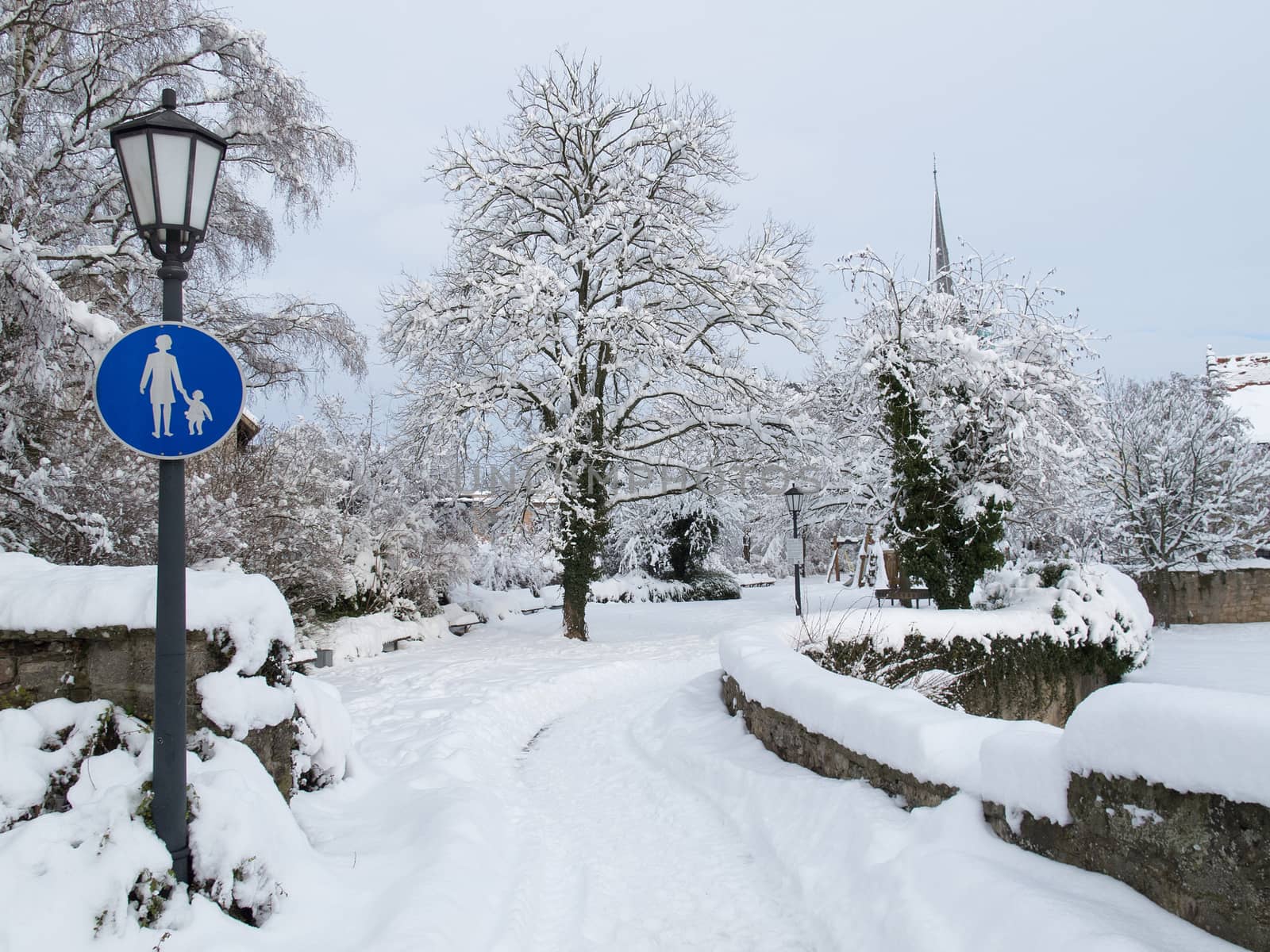 Snowy park with footpath and traffic sign for pedestrians