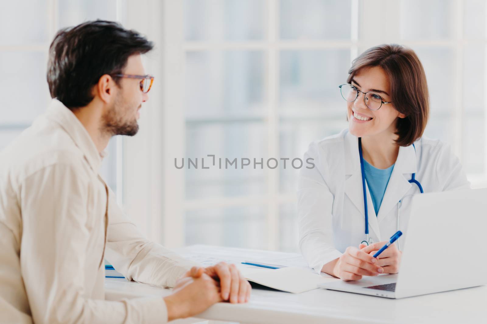 Skilled professional female general practitionist explains diagnosis and consults patient, demonstrates information in laptop, pose in clinical office, discuss scan results in diagnostic center by vkstock