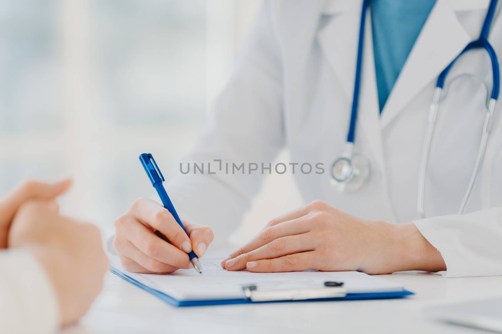 Unrecognizable woman doctor writes down in clipboard, makes prescription for patient, records data for analysis, wears white gown. Close up, focus on hands. Medicine, insurance, health care concept by vkstock