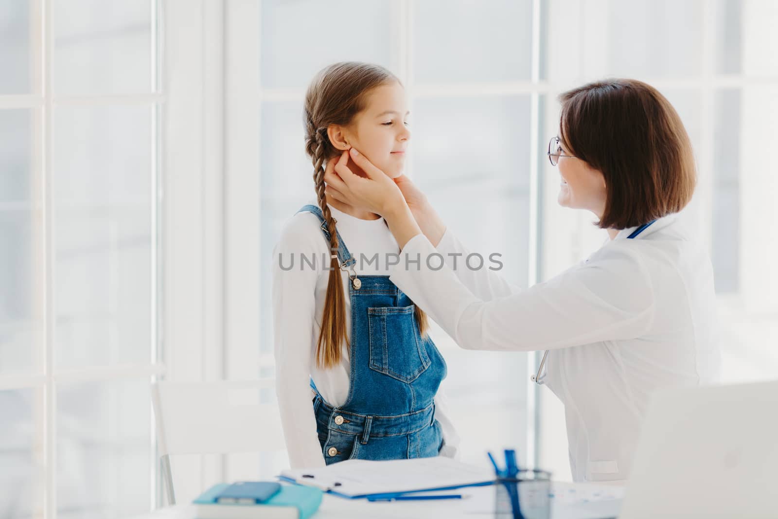 Photo of female pediatrician examines childs throat, being professional skilled pediatrician, consults kid how to prevent tonsillitis, gives good treatment and care. Medical checkup concept. by vkstock