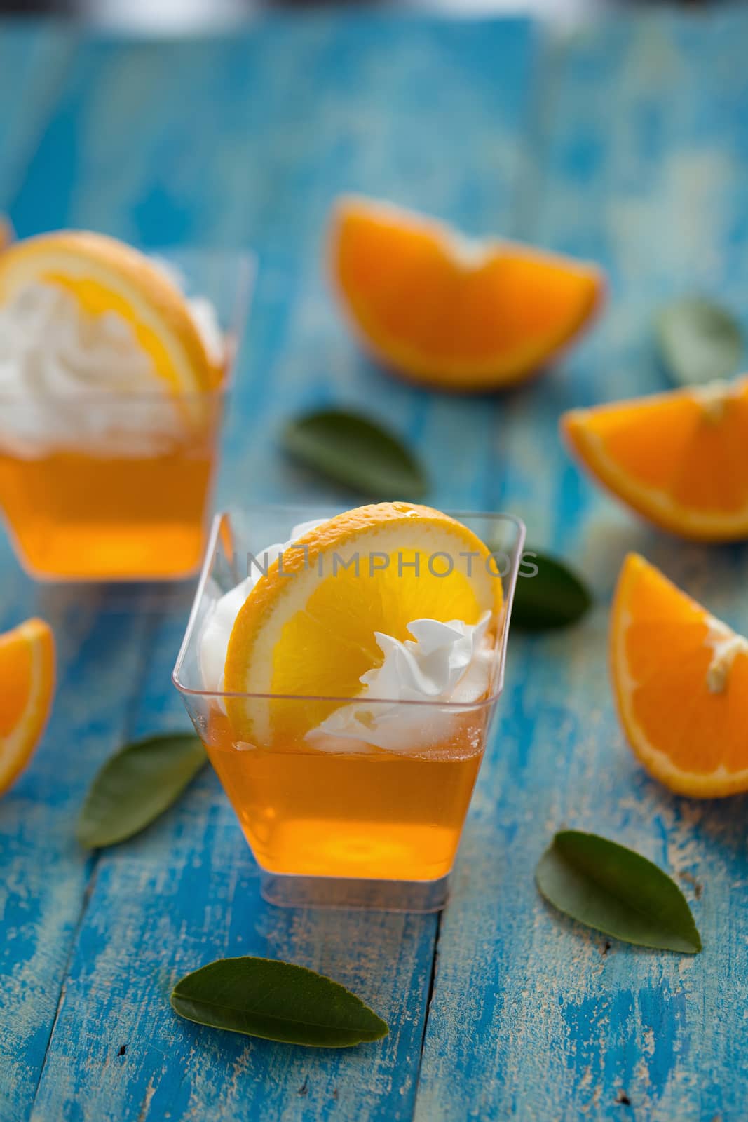 Orange jelly in a cup with whipped cream and orange sliced on blue wooden background.