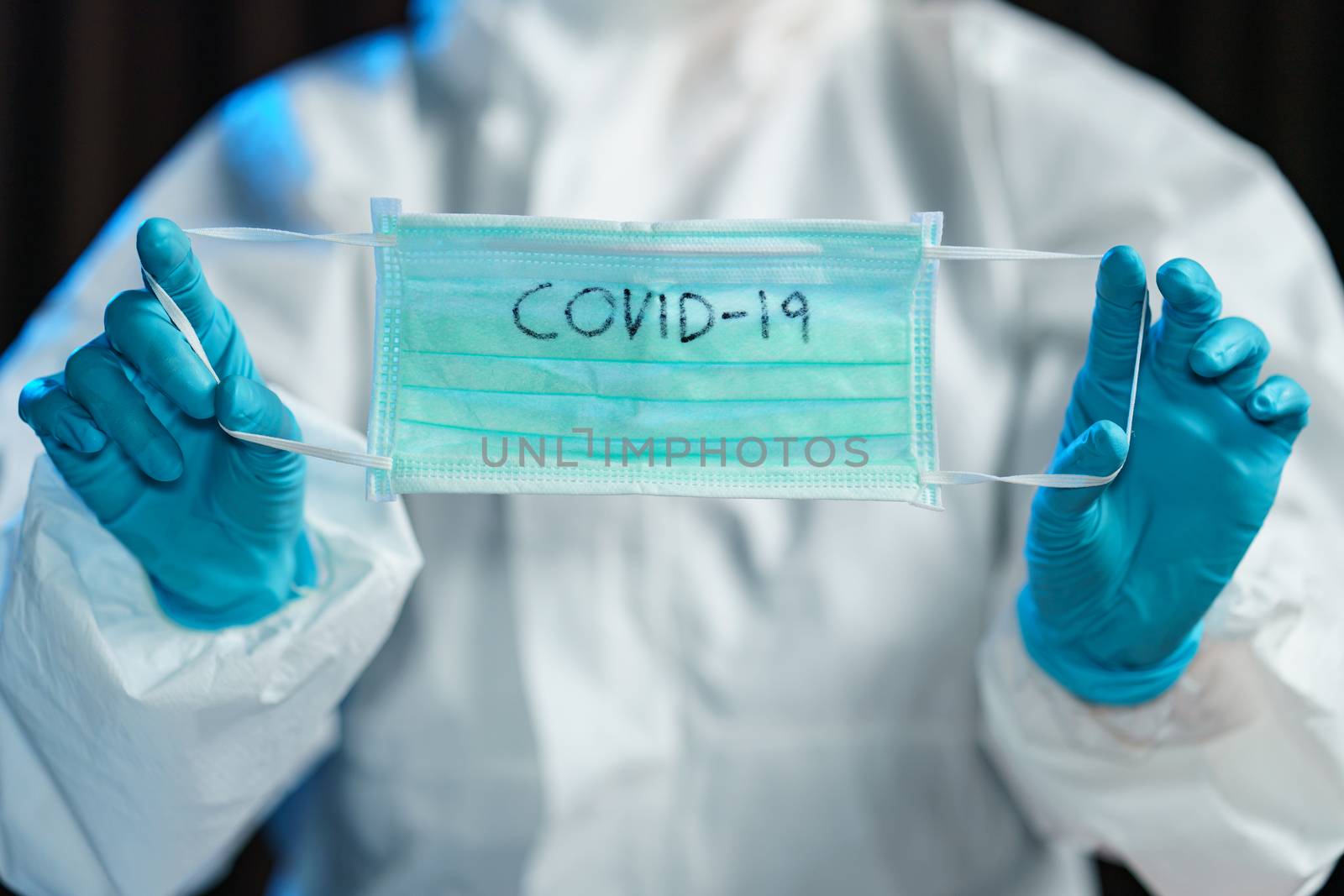 Scientist in hazmat suit, hand holding protective face mask with text covid-19.