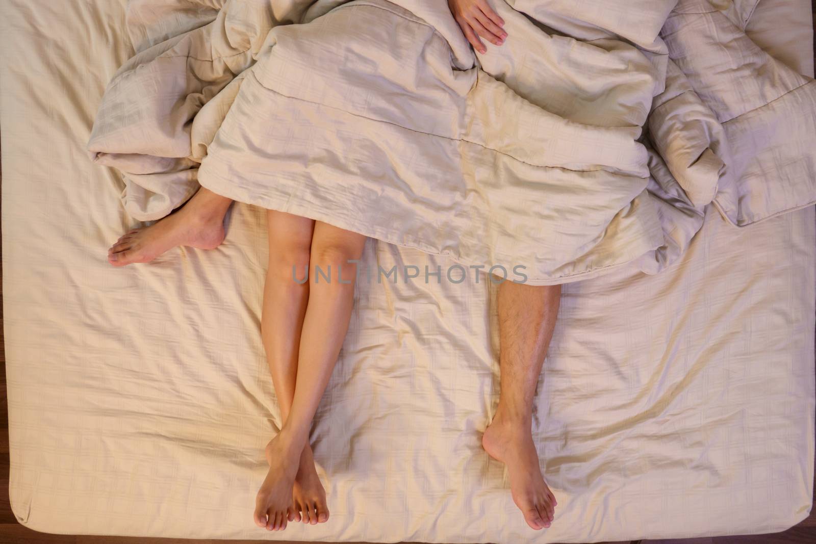 Close up of male and female feet on a bed having sex under sheets in the bedroom.