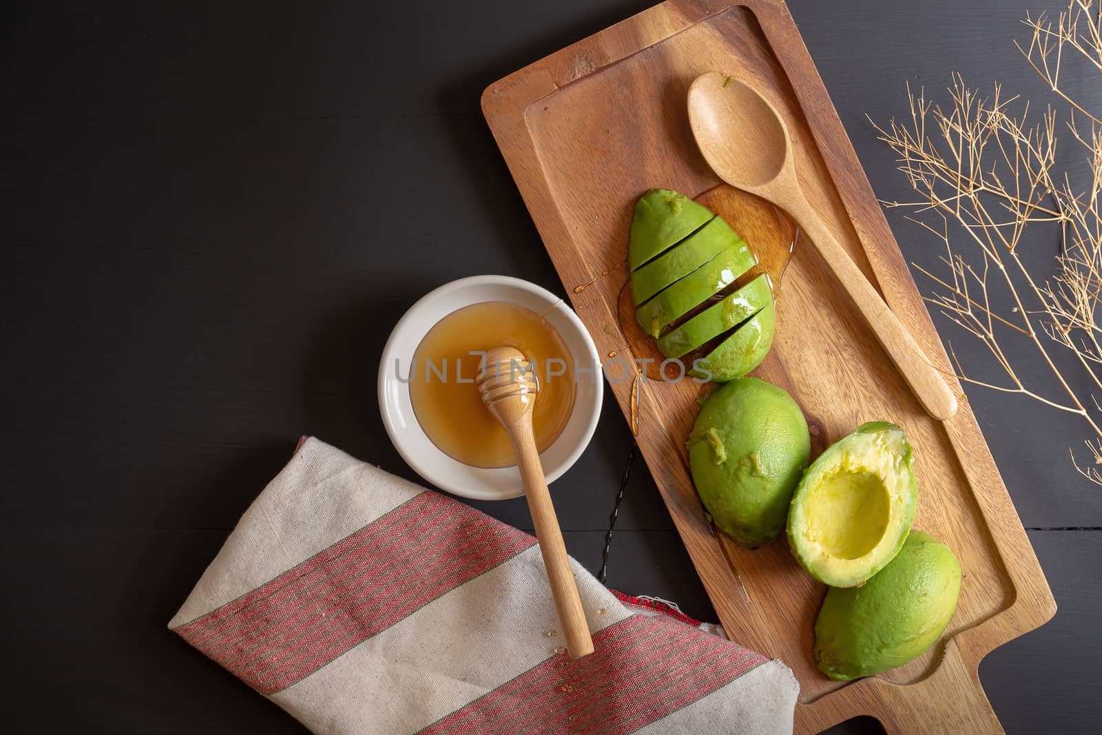 Fresh organic avocado sliced in half and honey on black wooden t by kaiskynet