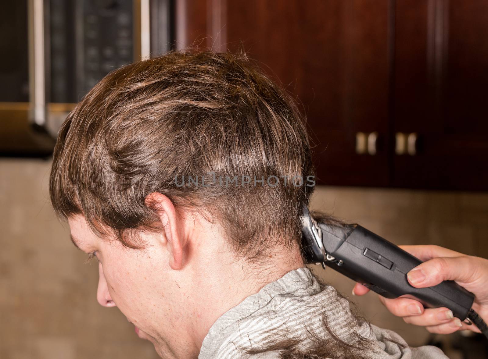Caucasian man having hair cut in kitchen with towel around his shoulders by steheap
