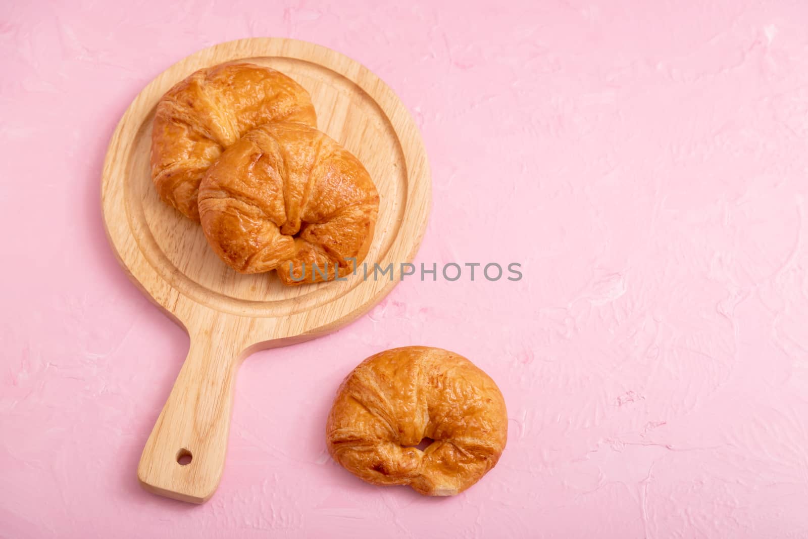 Top view croissants 2 pieces in the wooden board and one piece on the pink background and texture.