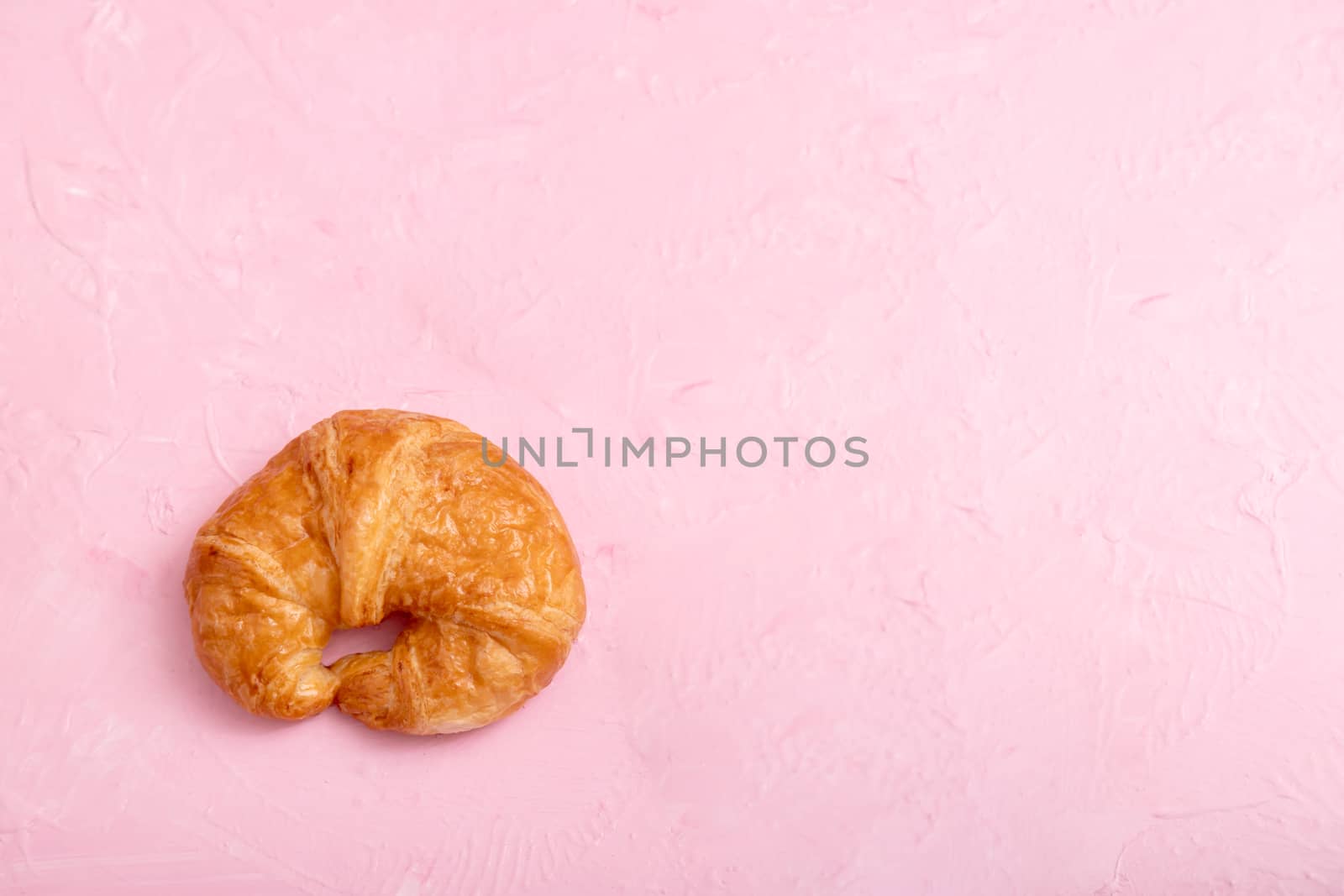 Top view a croissant on the pink background and texture.