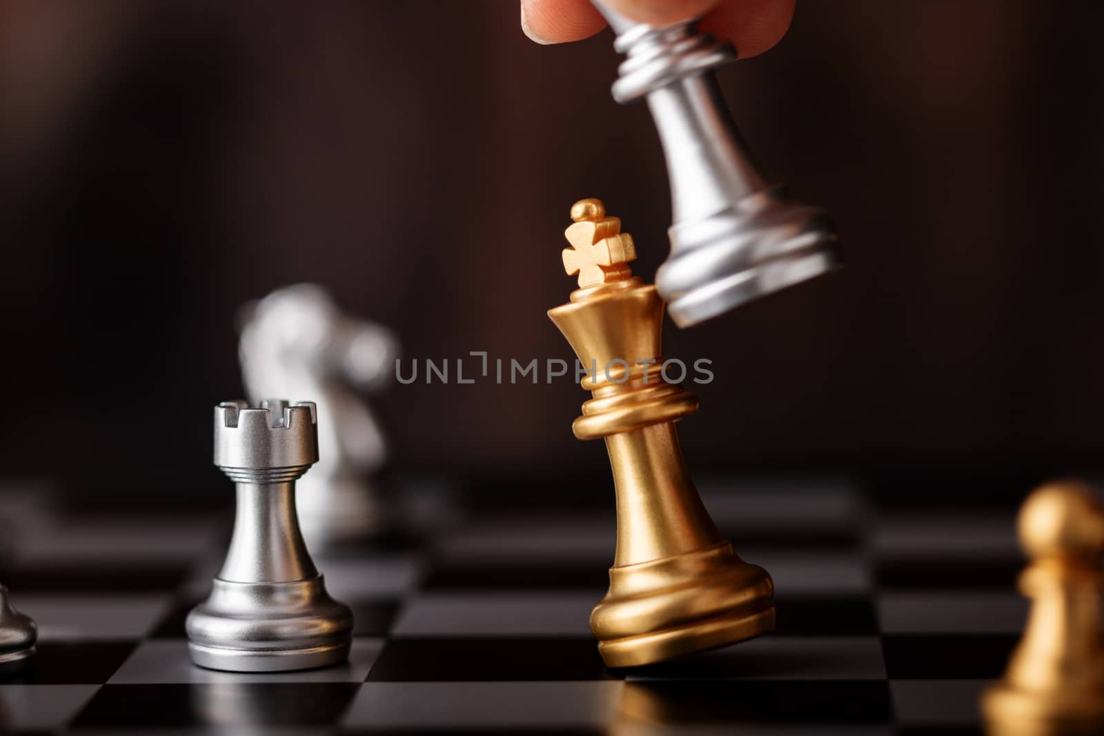 hand holding silver king attack gold leader in game on the chessboard