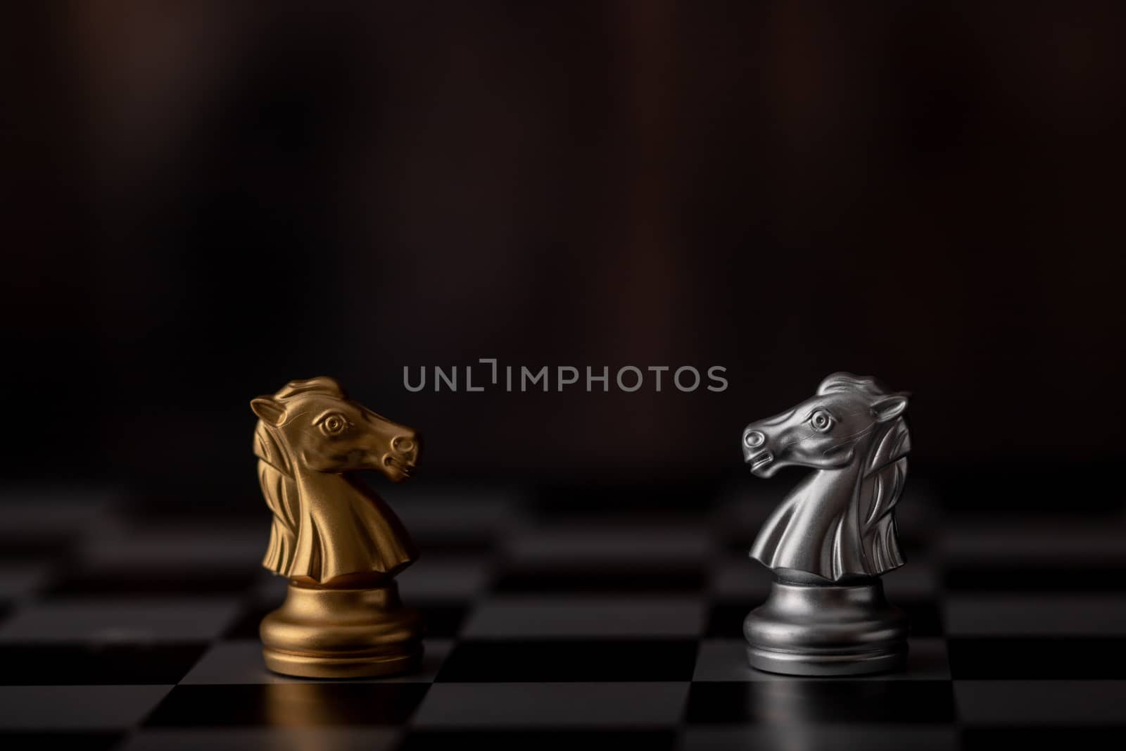 silver and gold horse of the chess in the game on board with wooden background.