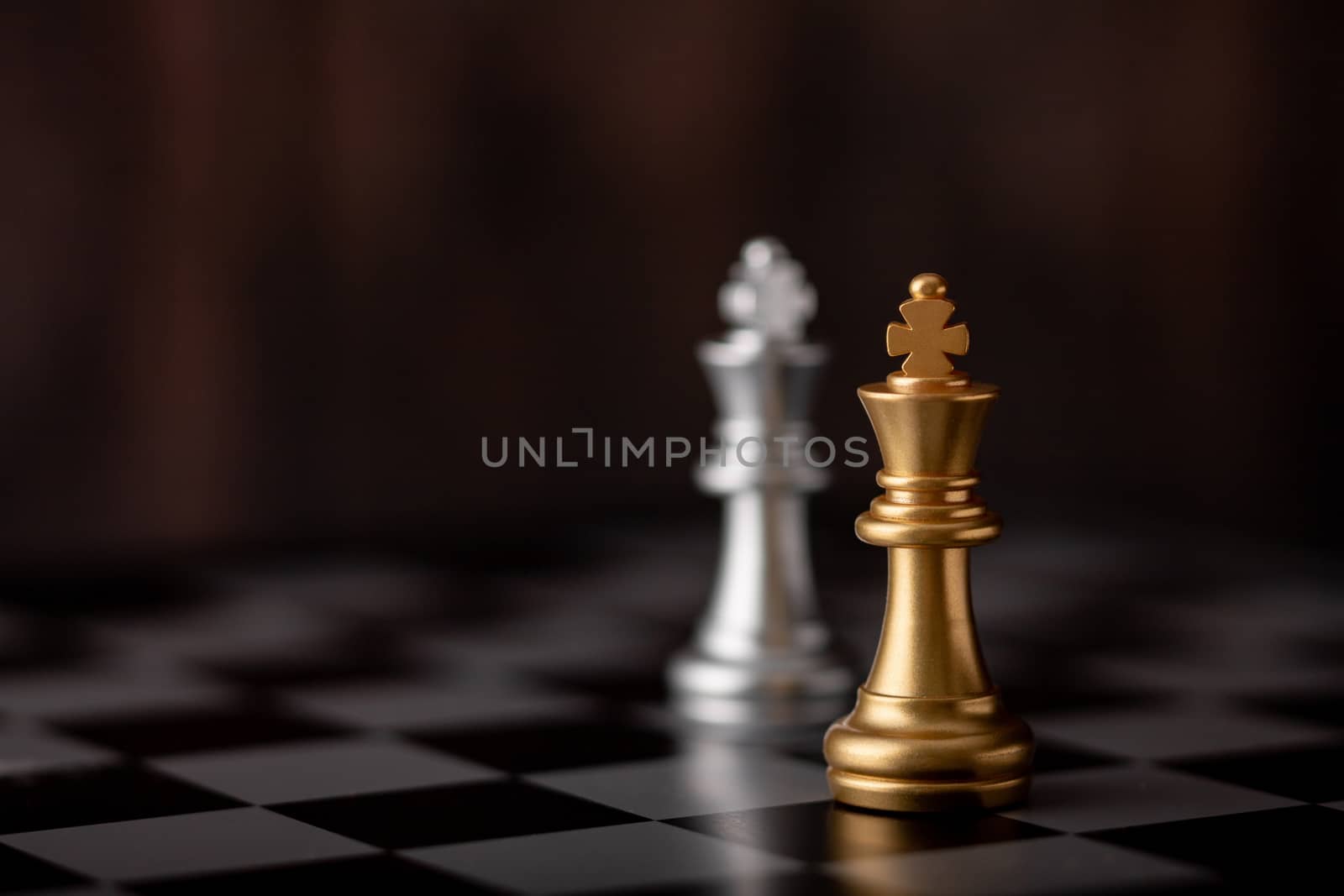 silver and gold king of the chess in the game on board with wooden background.