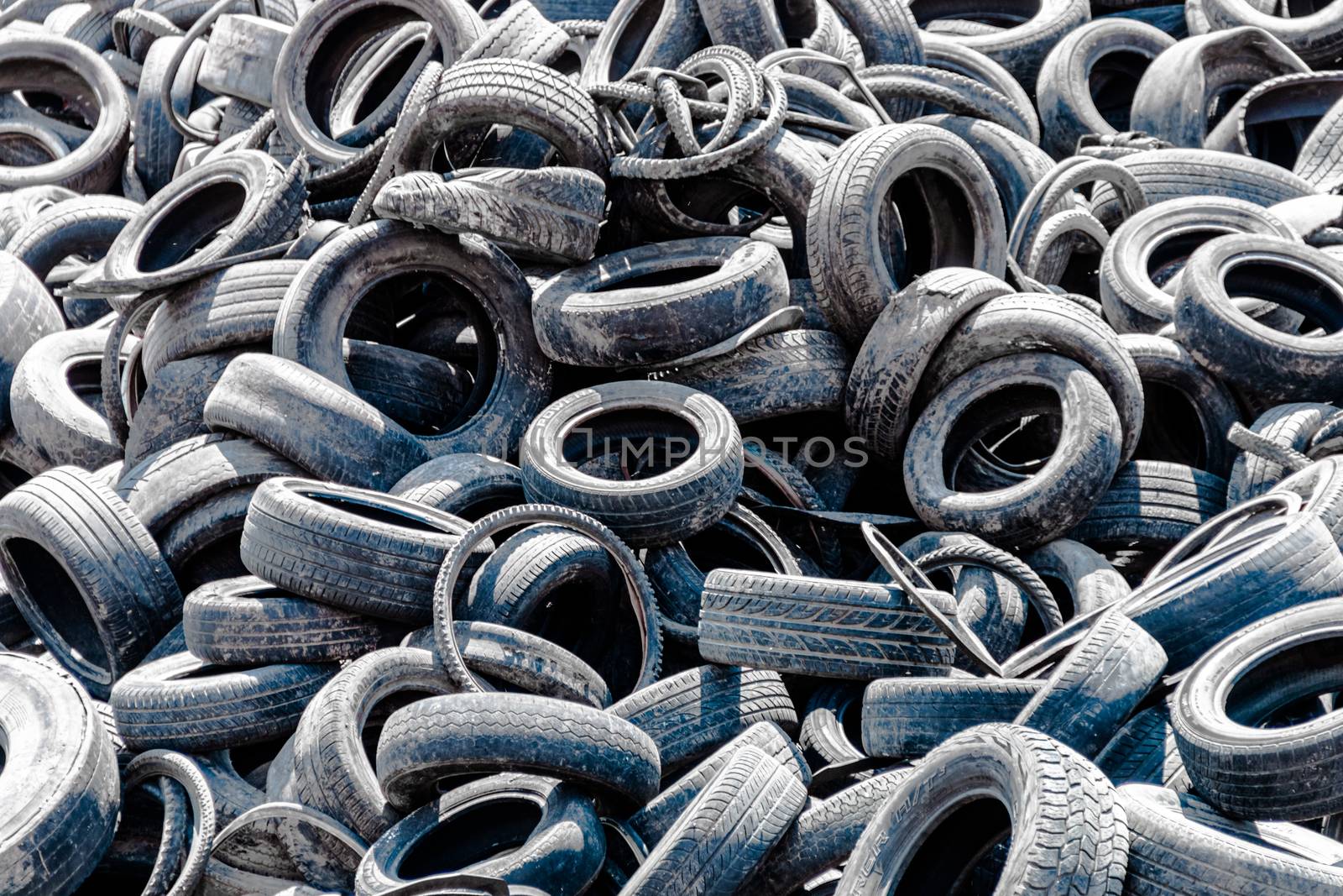 Assorted pile of old and used automotive road tires, showing a variety of tread patterns in a tires shop back yard. No people. by leo_de_la_garza