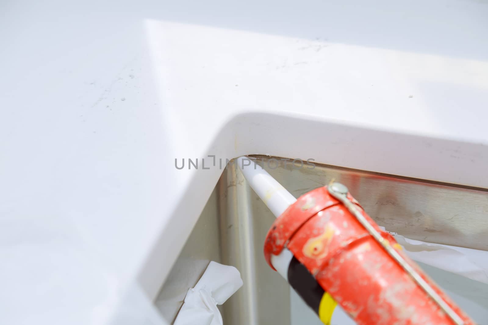 Worker installing granite sink in kitchen silicone sealant by ungvar