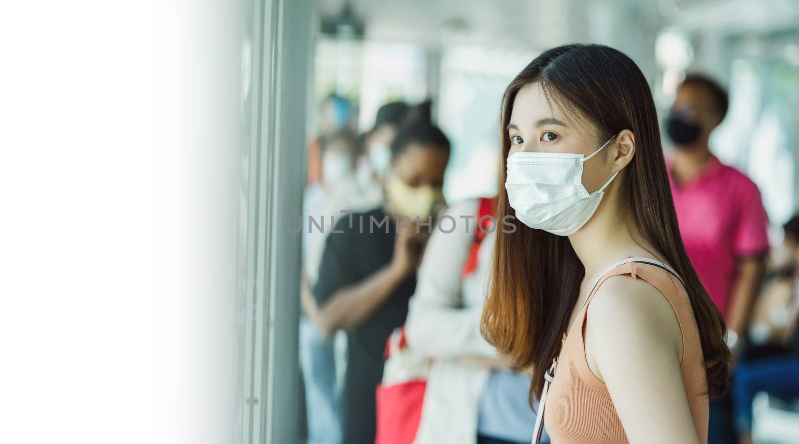 Young Asian woman passenger wearing surgical mask and waiting bus at station with crowned people when traveling in big city at Covid outbreak, Infection and Pandemic concept