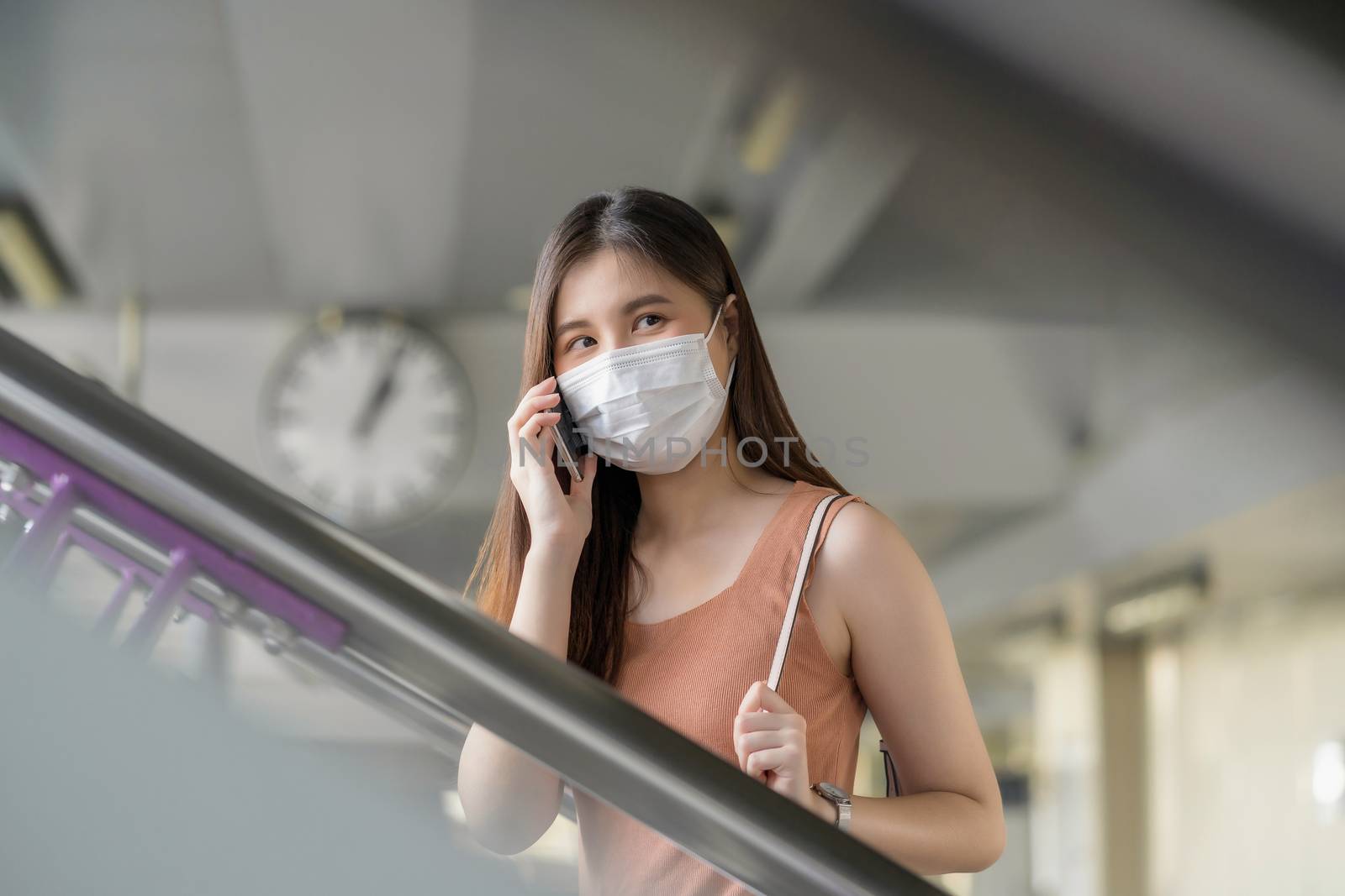 Young Asian woman passenger wearing surgical mask and using mobile phone for talking when walking up the stairs in subway station while traveling at Covid19 outbreak, Infection and Pandemic concept