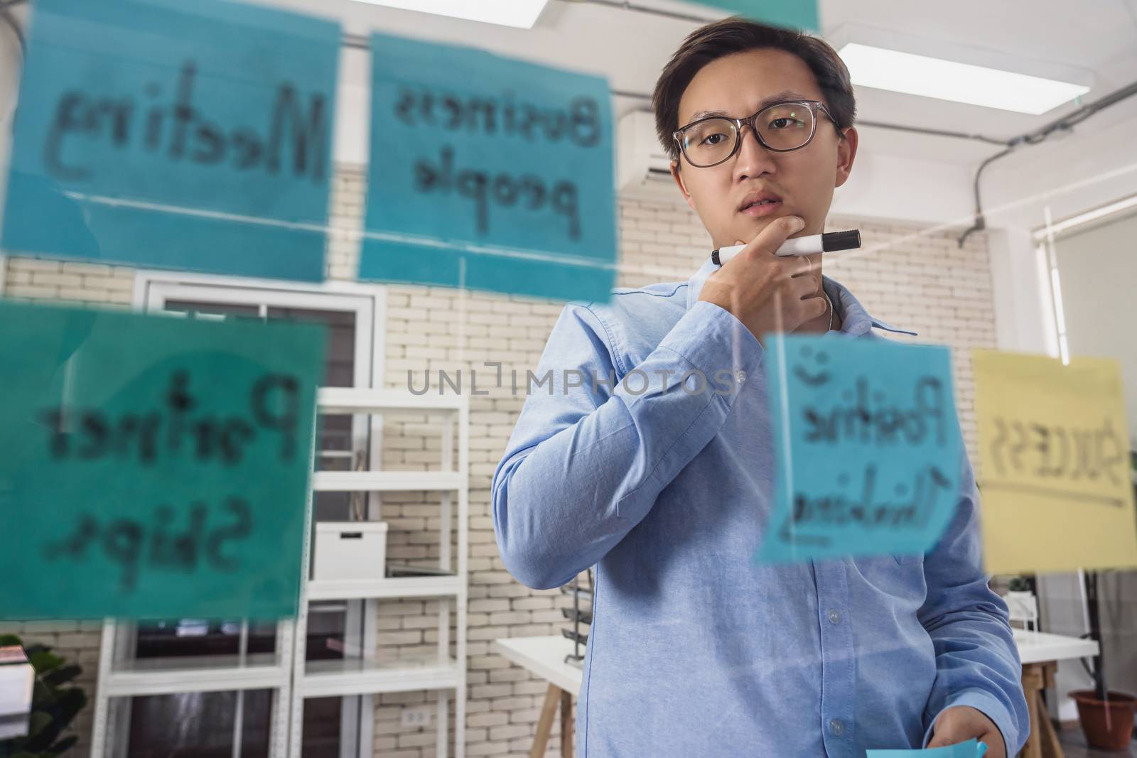 Asian Business man concentrating and thinking before putting the post it on the mirror in concern action at office or coworking space, startup and entrepreneur,workshop and strategy concept