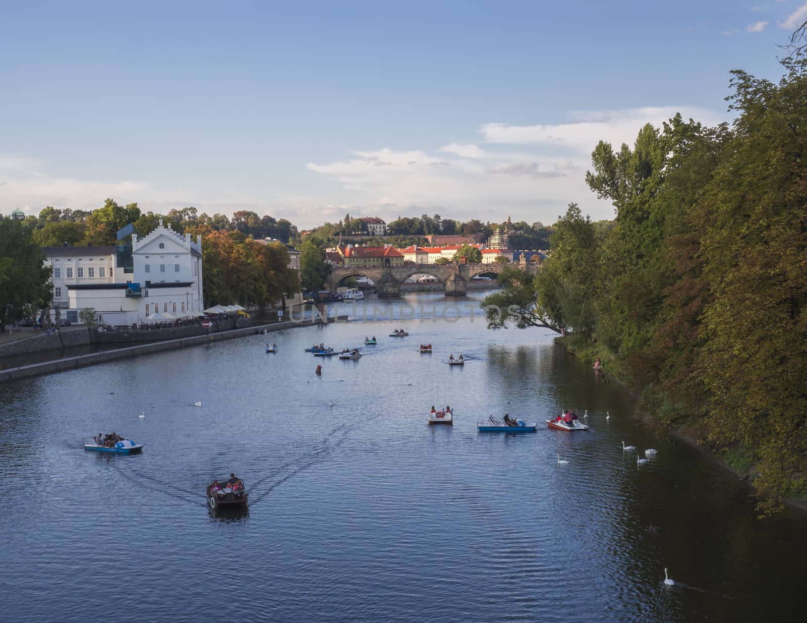 panorama of Charles bridge over Vltava river and houses of Old Town, Prague, Czech Republic, golden hour light, summer sunny day, tourists relaxing on pedal boats.