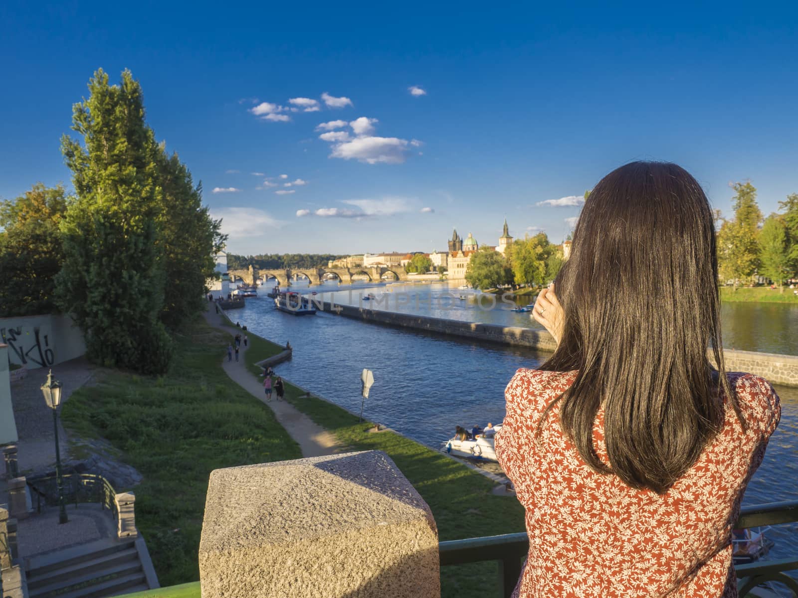 young woman, taking picture with her cell phone from Legion Bridge with view on Kampa island, Vltava river, Prague Castle, Old Town, summer sunny afternoon, Czech Republic, Prague, summer sunny day.