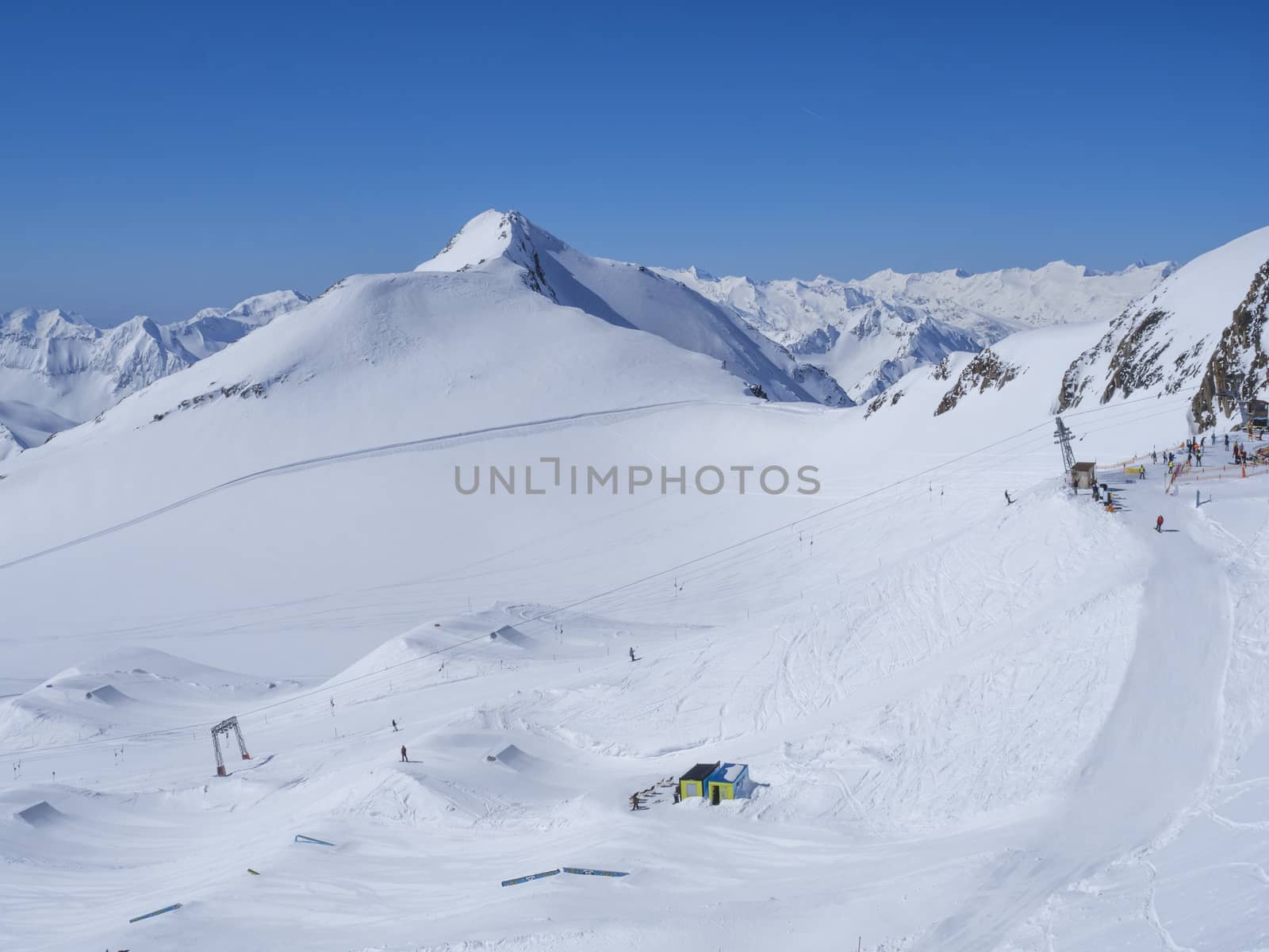 Winter landscape with snow covered mountain slopes and pistes with skiers enjoying spring sunny day at ski resort Stubai Gletscher, Stubaital, Tyrol, Austrian Alps.