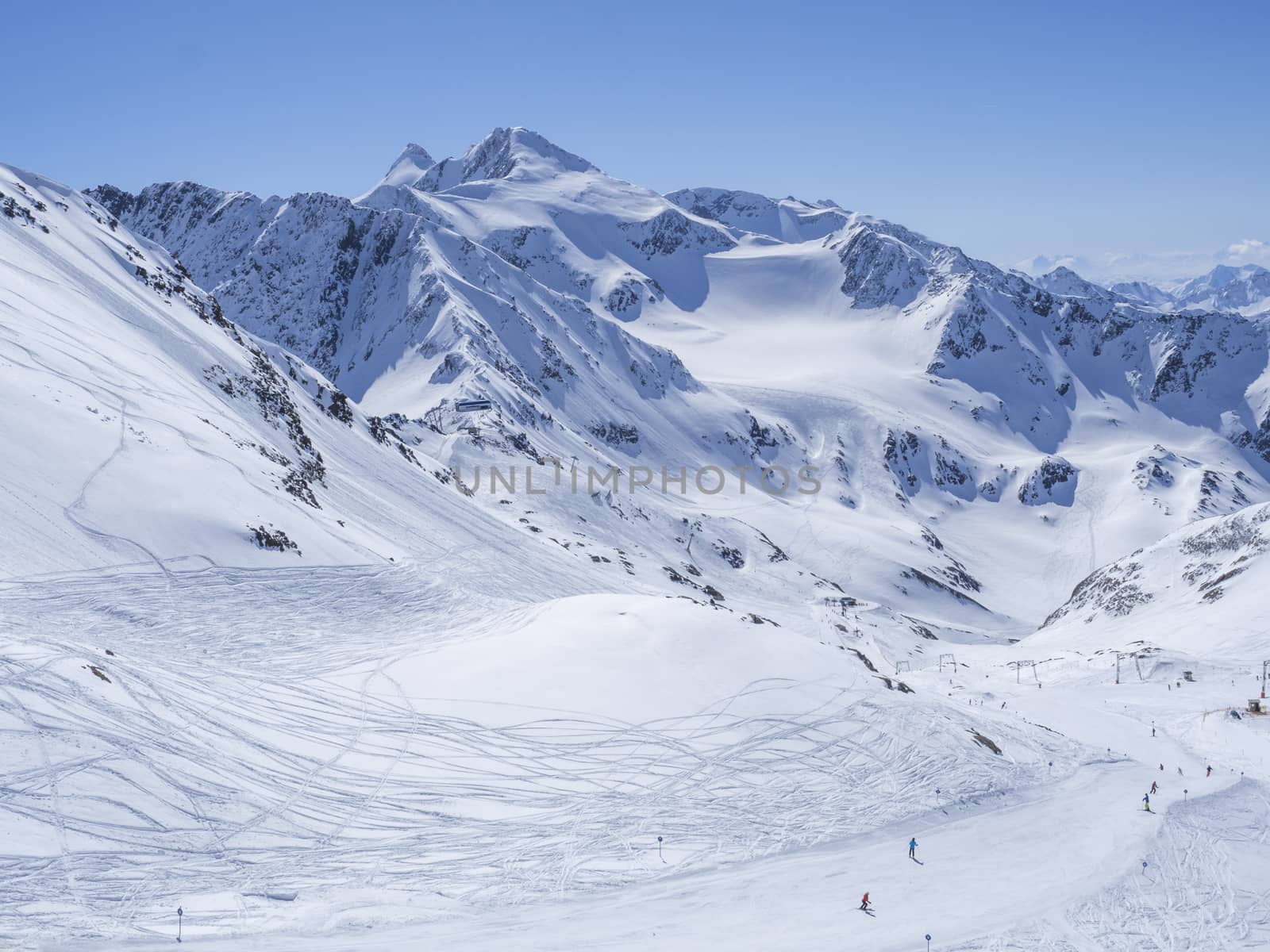 Winter landscape with snow covered mountain slopes and pistes with skiers enjoying spring sunny day at ski resort Stubai Gletscher, Stubaital, Tyrol, Austrian Alps.