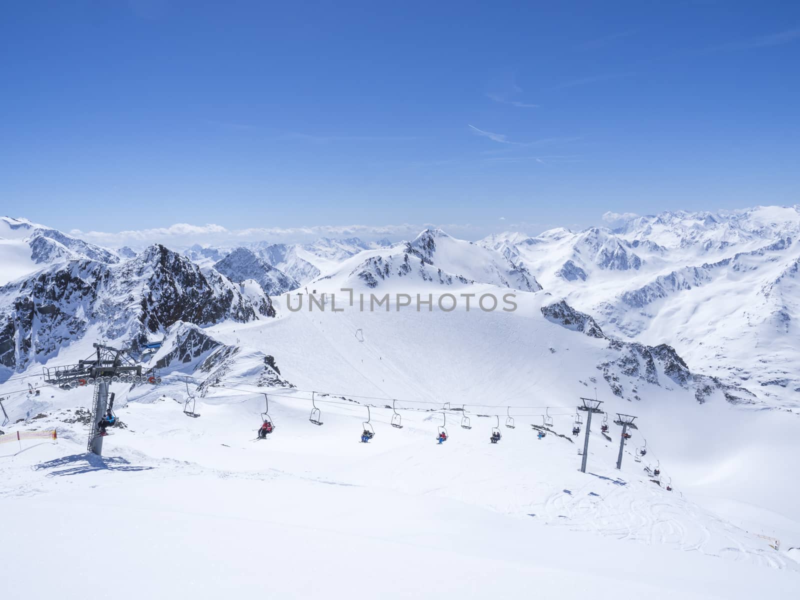 Scenic view from top of Wildspitze on winter landscape with snow covered mountain slopes and pistes and skiers on chair lift at Stubai Gletscher ski resort at spring sunny day. Blue sky background. Stubaital, Tyrol, Austrian Alps