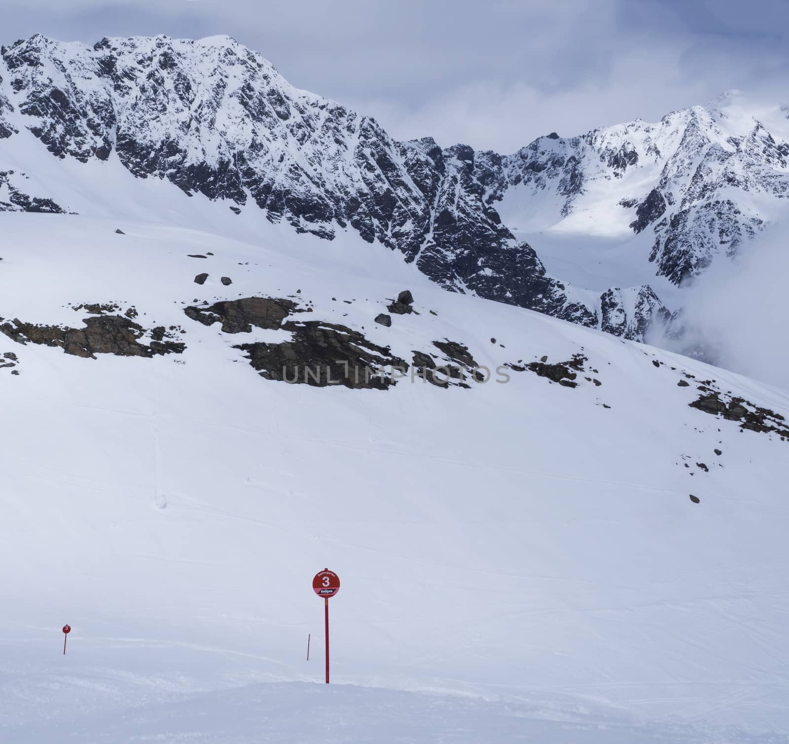 Winter landscape with empty red piste sign, snow covered mountain slopes, spring sunny day at ski resort Stubai Gletscher, Stubaital, Tyrol, Austrian Alps