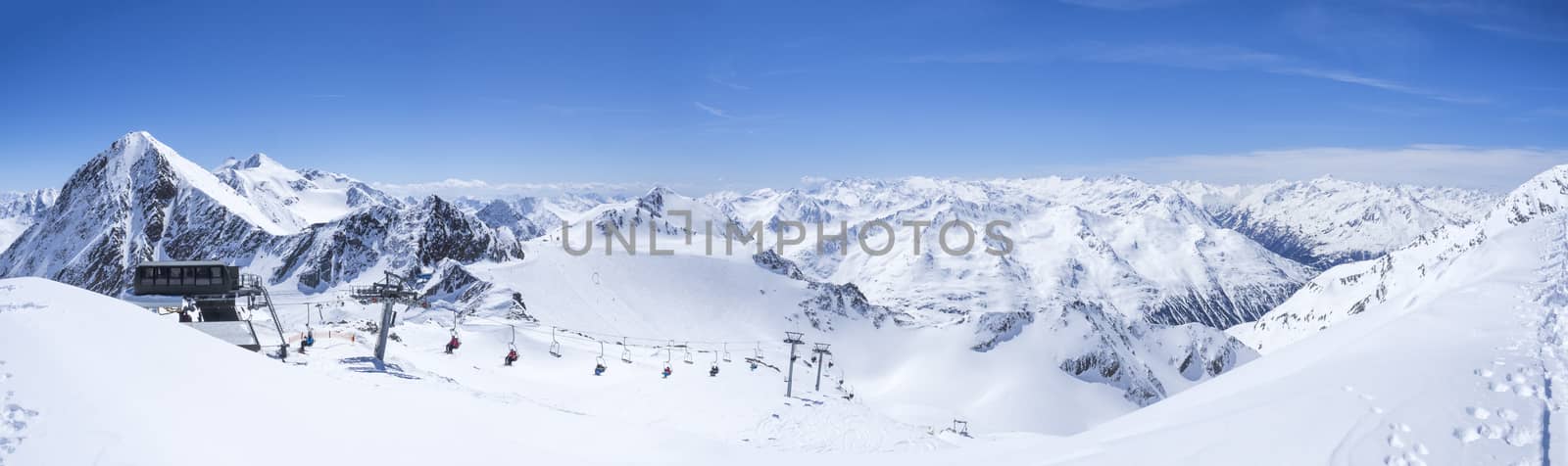 Panoramic landscape view from top of Wildspitz on winter landscape with snow covered mountain slopes and pistes and skiers on chair lift at Stubai Gletscher ski resort at spring sunny day. Blue sky background. Stubaital, Tyrol, Austrian Alps by Henkeova