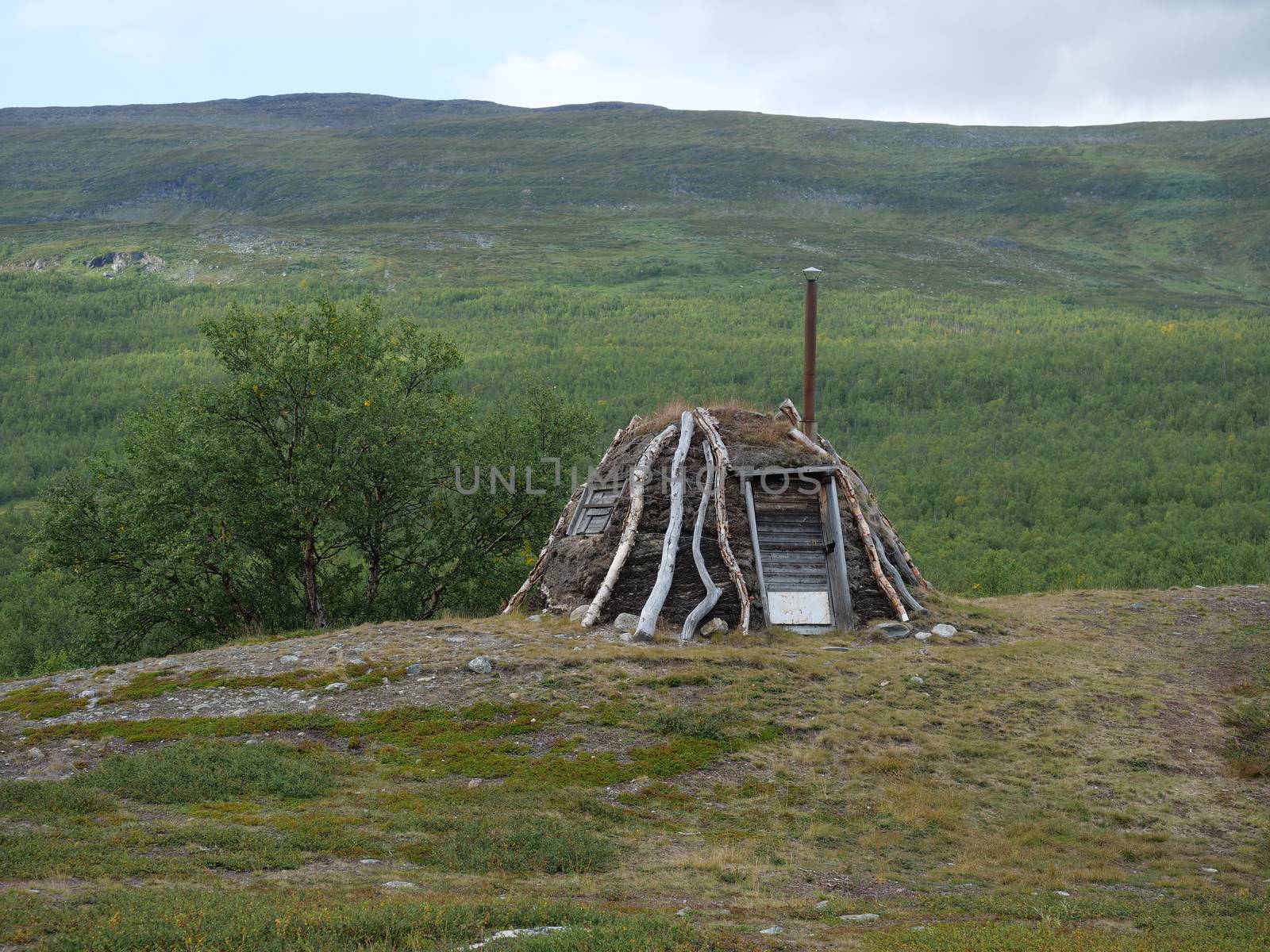 Abadoned Sami hut Goathi in green hills landscape of Abisko National Park. Goahti is Lappish traditional dwelling made from fabric, peat moss and timber. Lapland, Northern Sweden on Kungsleden trail. Summer sunny day.