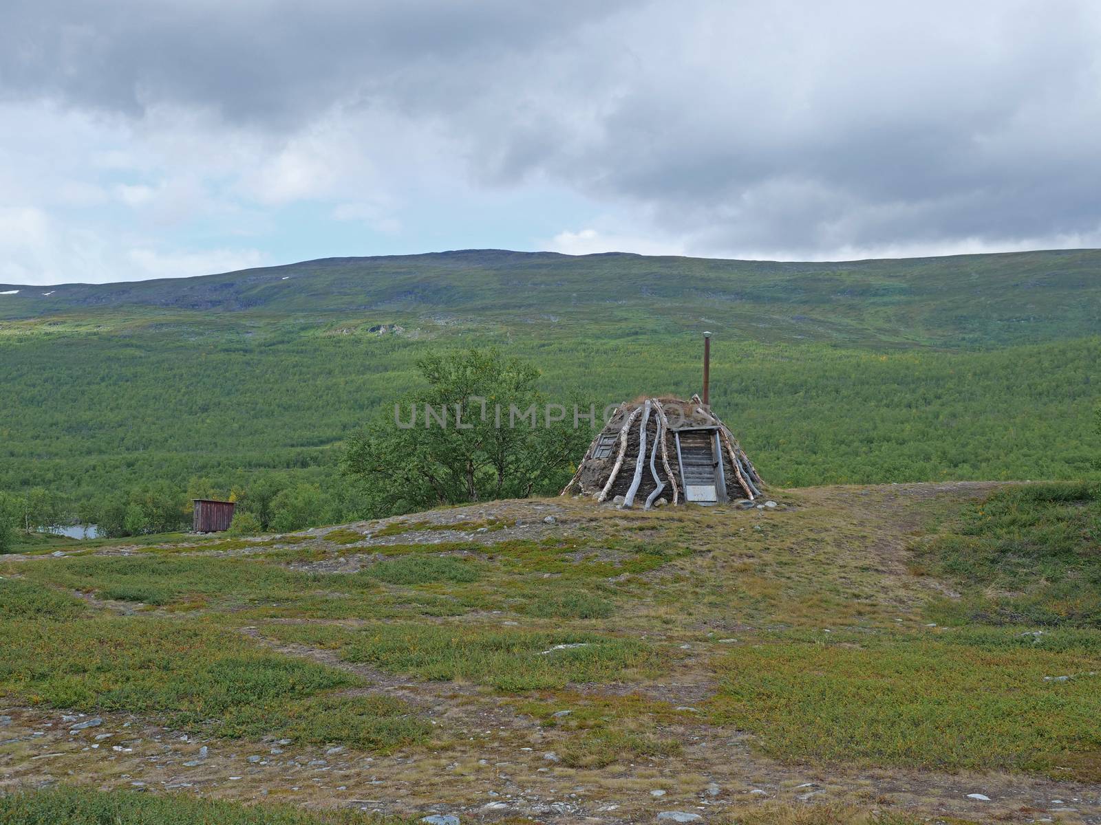 Abadoned Sami hut Goathi in green hills landscape of Abisko National Park. Goahti is Lappish traditional dwelling made from fabric, peat moss and timber. Lapland, Northern Sweden on Kungsleden trail. Summer sunny day.