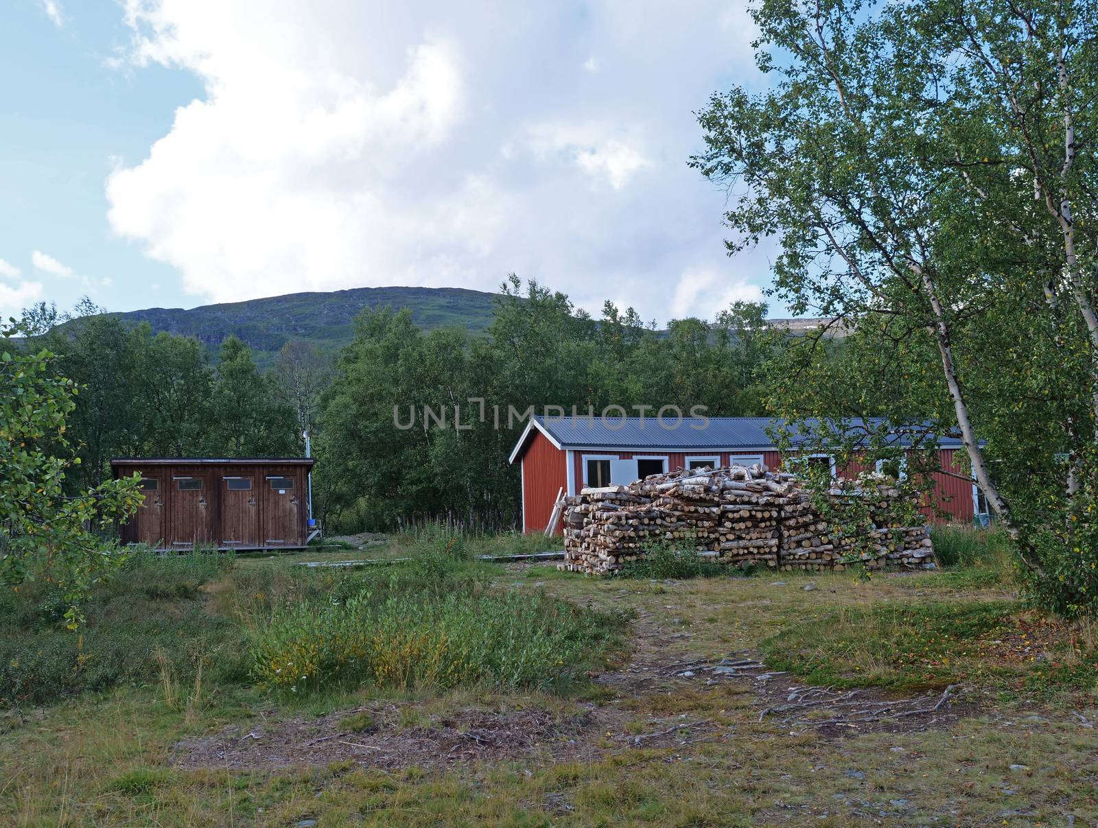 Red building of AbiskoJaure STF mountain hut. Green hills, birch forest on the Kungsleden Trail, summer blue sky.