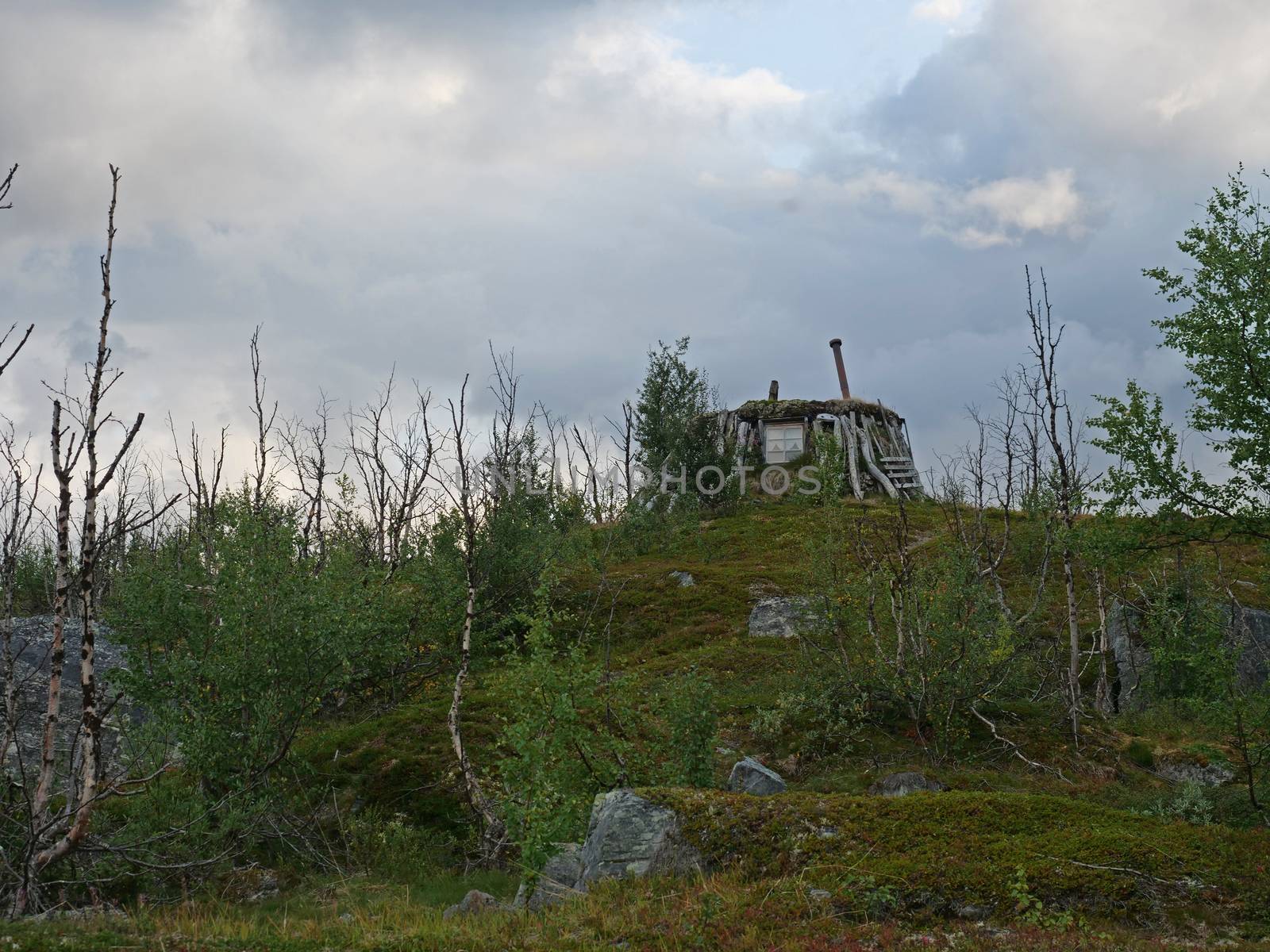 Abadoned Sami hut Goathi in green hills landscape of Abisko National Park. Goahti is Lappish traditional dwelling made from fabric, peat moss and timber. Lapland, Northern Sweden on Kungsleden trail. Summer sunny day.