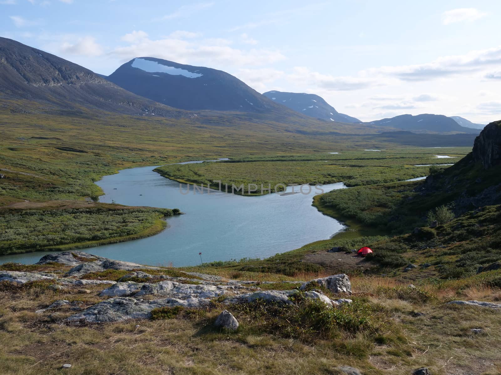 Lapland nature landscape with blue glacial lake Allesjok near Alesjaure, birch tree forest, snow capped mountains and lonely red tent, Northern Sweden, at Kungsleden hiking trail. Summer sunny day.