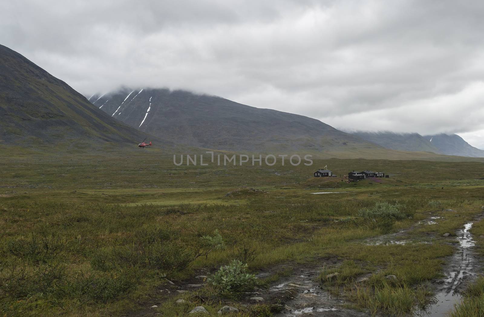 Red helicopter supply Hikers at Mountain Lodge Salka STF hut. Lapland mountain ladscape on summer cloudy day