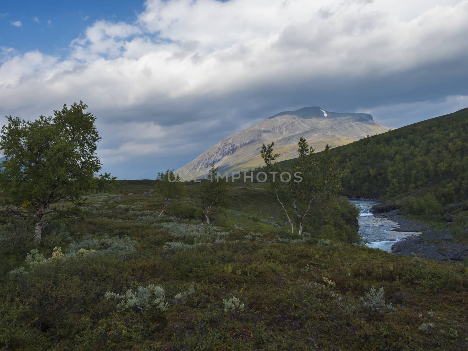 Lapland nature landscape with blue glacial river and Alesjaure STF Mountain cabin hut, birch tree forest, snow capped mountains and lonely red tent, Northern Sweden, at Kungsleden hiking trail. Summer sunny day.