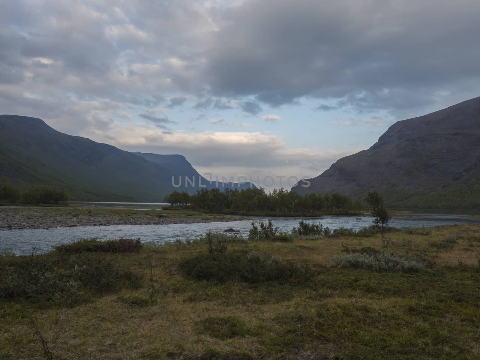 Beautiful wild Lapland nature landscape with blue glacial river, Kaitumjaure lake, birch tree forest and mountains. Northern Sweden summer at Kungsleden hiking trail. Blue sky dramatic sunset clouds. by Henkeova