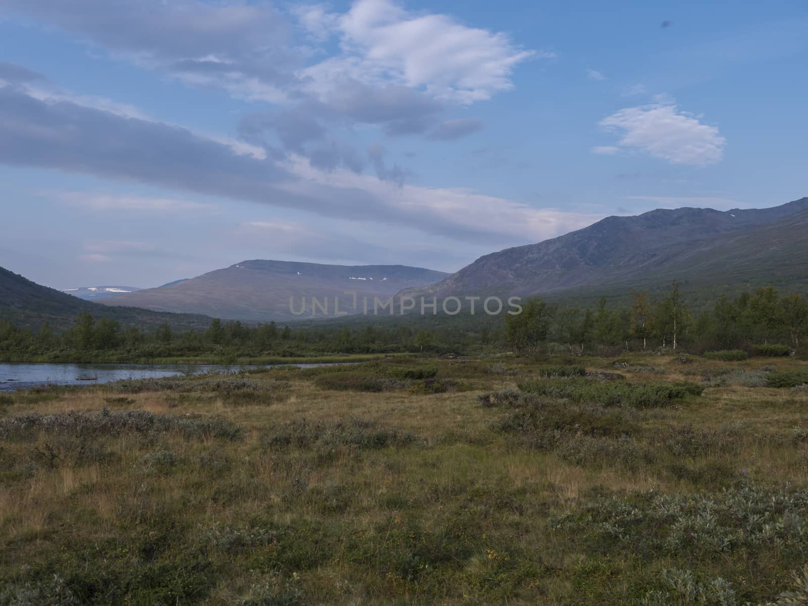 Beautiful wild Lapland nature landscape with blue Tjaktjajakka river, Kaitumjaure, birch tree forest and mountain Sanjartjakka. Northern Sweden summer at Kungsleden hiking trail. Blue sky background by Henkeova