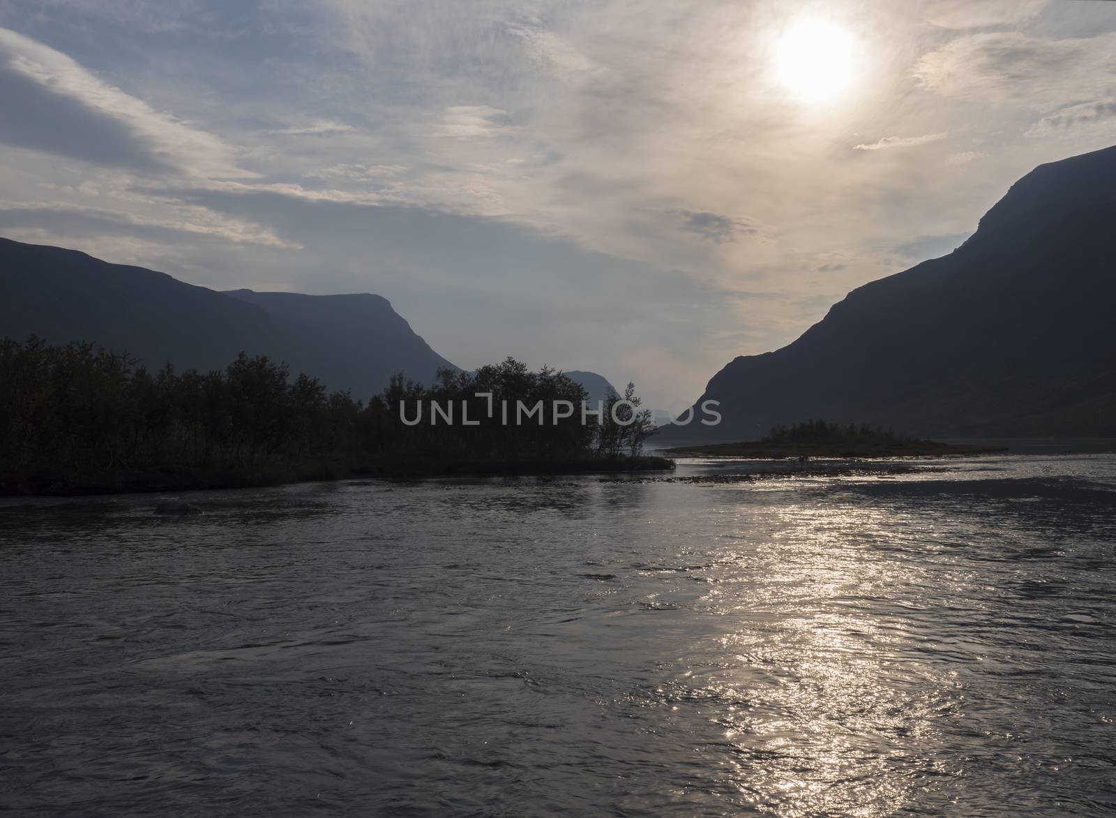 Confluence of wild Tjaktjajakka river and Kaitumjaure lake with small birch tree forest island and mountains. Lapland nature landscape, summer sunset at Kungsleden hiking trail. by Henkeova