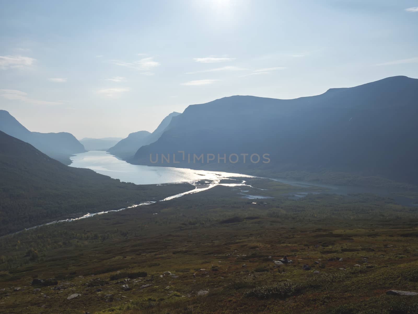 Aerial view from mountain Sanjartjakka on wild Lapland landscape with Tjaktjajakka river, Kaitumjaure lake, birch tree forest and mountains. Northern Sweden summer. Blue sky background, backlight.