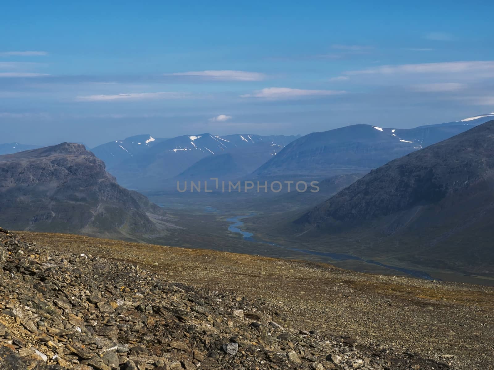 Aerial view from mountain Sanjartjakka on wild Lapland landscape with Tjaktjajakka river valley, and snow capped mountains. Northern Sweden summer. Blue sky background.