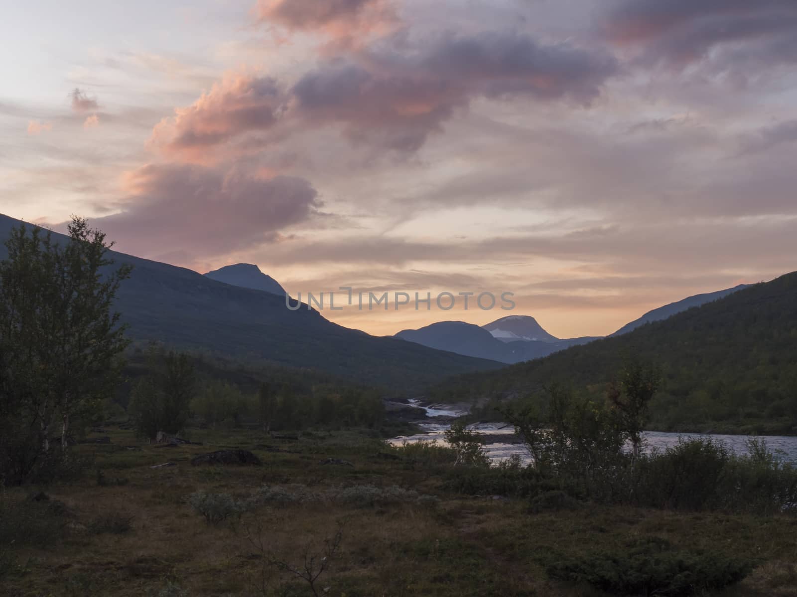 Wild Tjaktjajakka river and Kaitumjaure lake with waterfall cascade and mountains. Lapland nature landscape in summer, sunset pink clouds.
