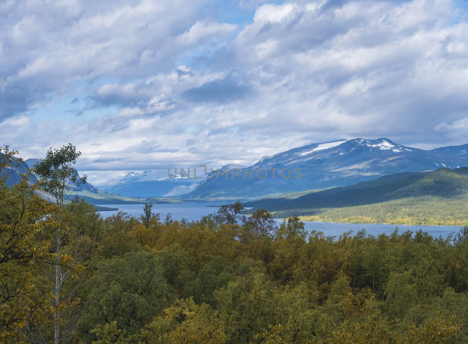 Lapland landscape with beautiful river Lulealven, snow capped mountain, birch tree and footpath of Kungsleden hiking trail near Saltoluokta, north of Sweden wild nature. Summer blue sky.
