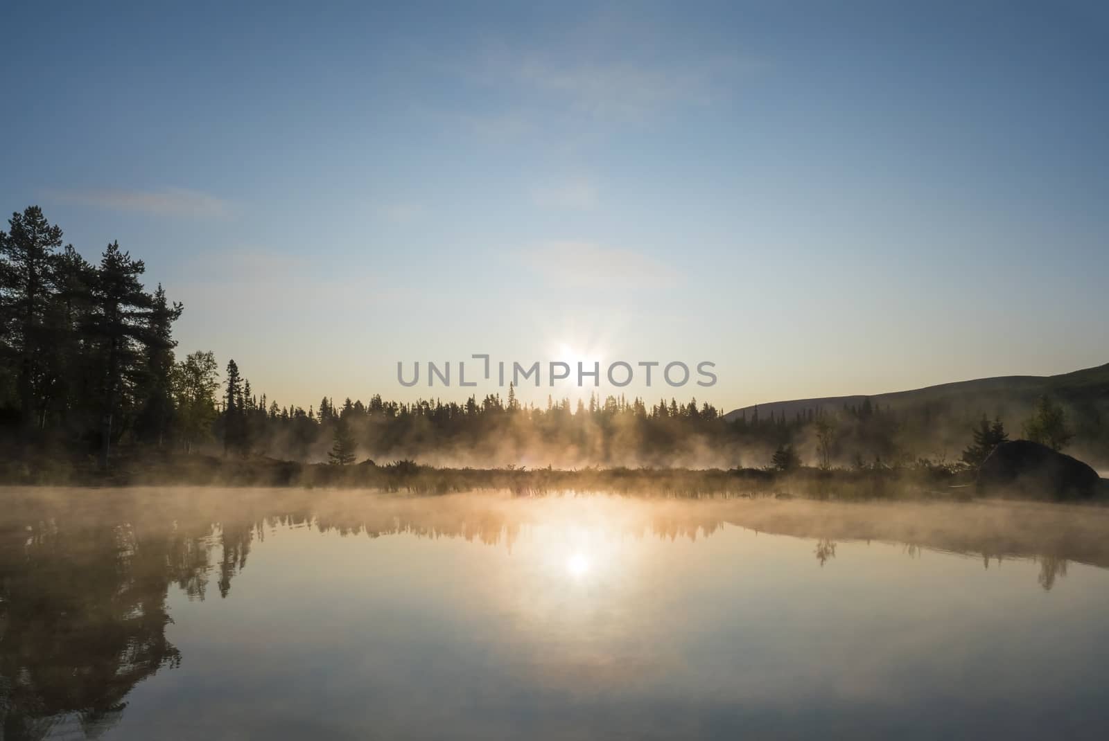 Beautiful morning orange sunrise over lake Sjabatjakjaure with haze mist in Sweden Lapland nature. Mountains, birch trees, spruce forest, rock boulders and grass. Sky, clouds and clear water. by Henkeova