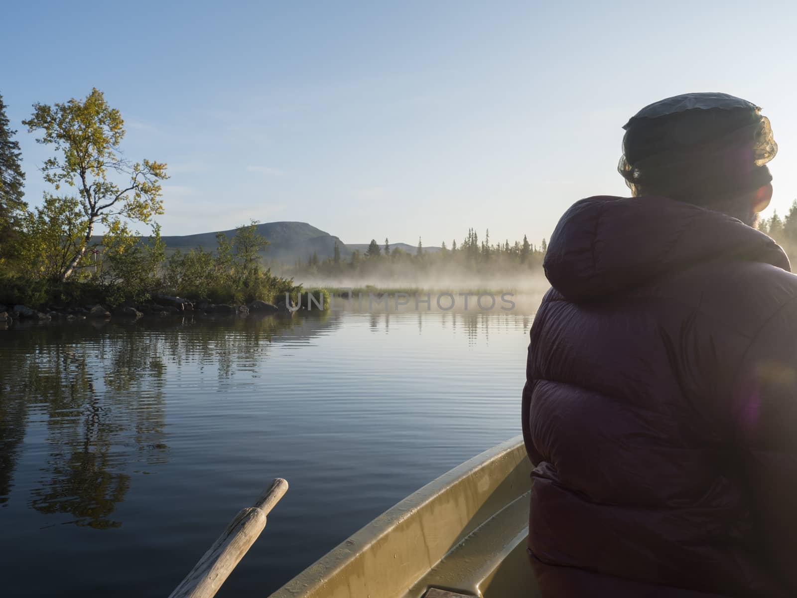 Fisherman man in rowing boat at lake Sjabatjakjaure in Beautiful sunny morning haze mist in Sweden Lapland nature. Mountains, birch trees, spruce forest. Blu sky and backlight by Henkeova