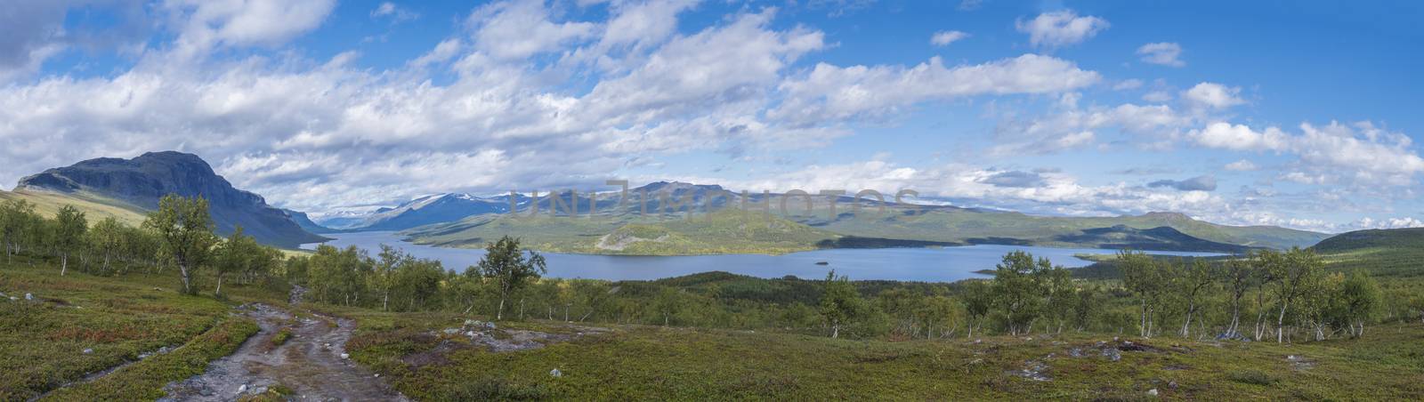 Panoramic landscape with beautiful river Lulealven, snow capped mountain, birch tree and footpath of Kungsleden hiking trail near Saltoluokta, north of Sweden, Lapland wild nature. Summer blue sky.