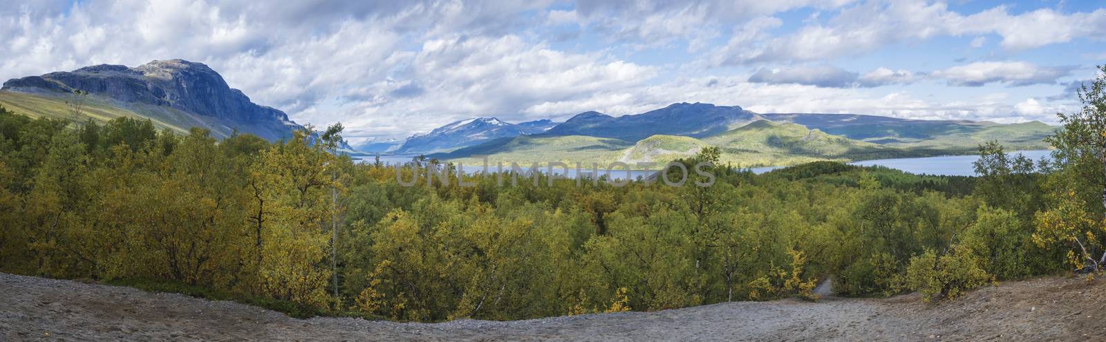 Panoramic landscape with beautiful river Lulealven, snow capped mountain and yellow birch tree. Kungsleden hiking trail near Saltoluokta, north of Sweden, Lapland wild nature. Early autumn blue sky.