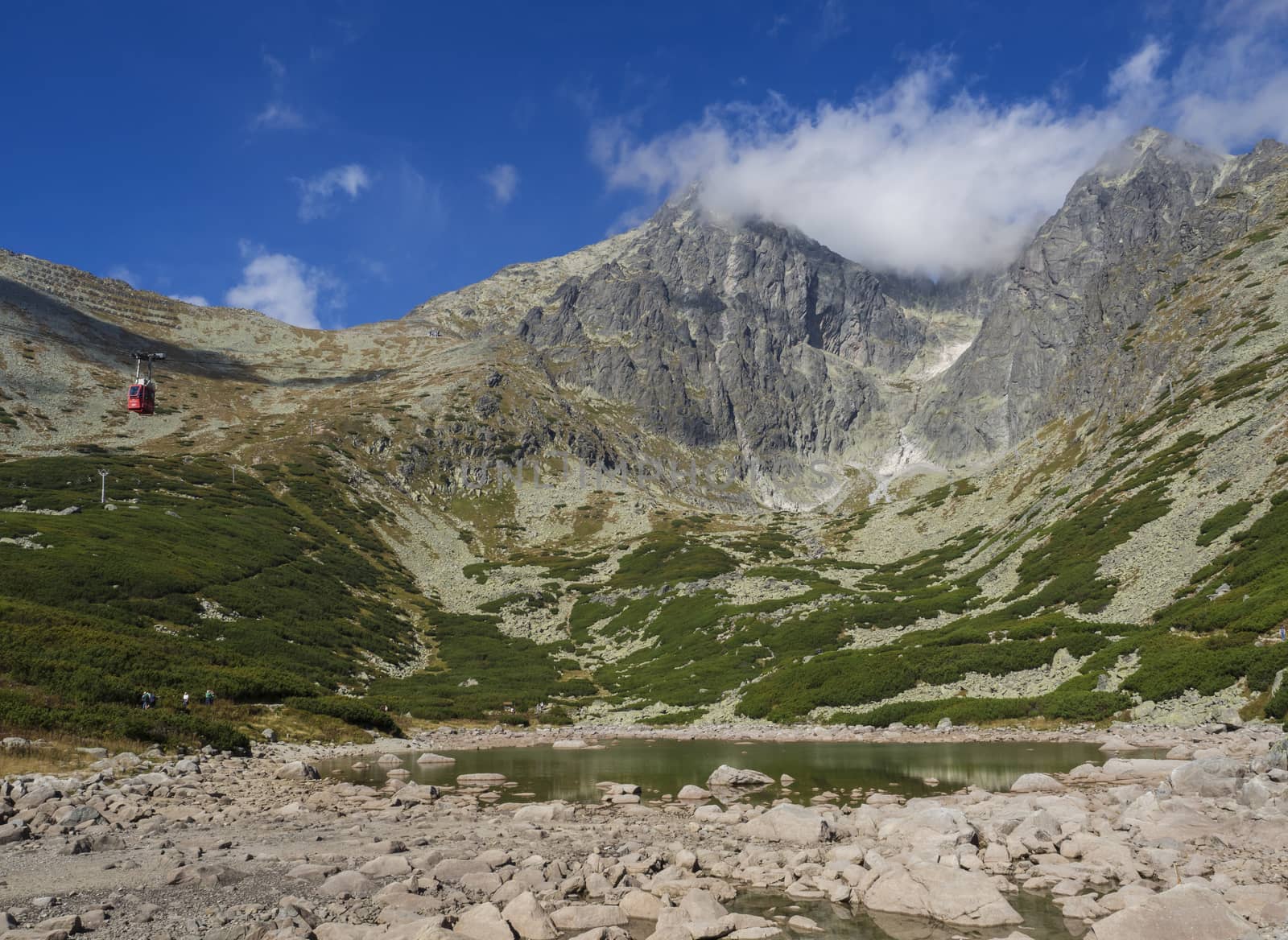 View on mountain Peak Lomnicky stit 2 634 m covered in clouds at Summer, in the High Tatras mountains of Slovakia with mountain lake Skalnate pleso and red cable car cabine, Vysoke Tatry.