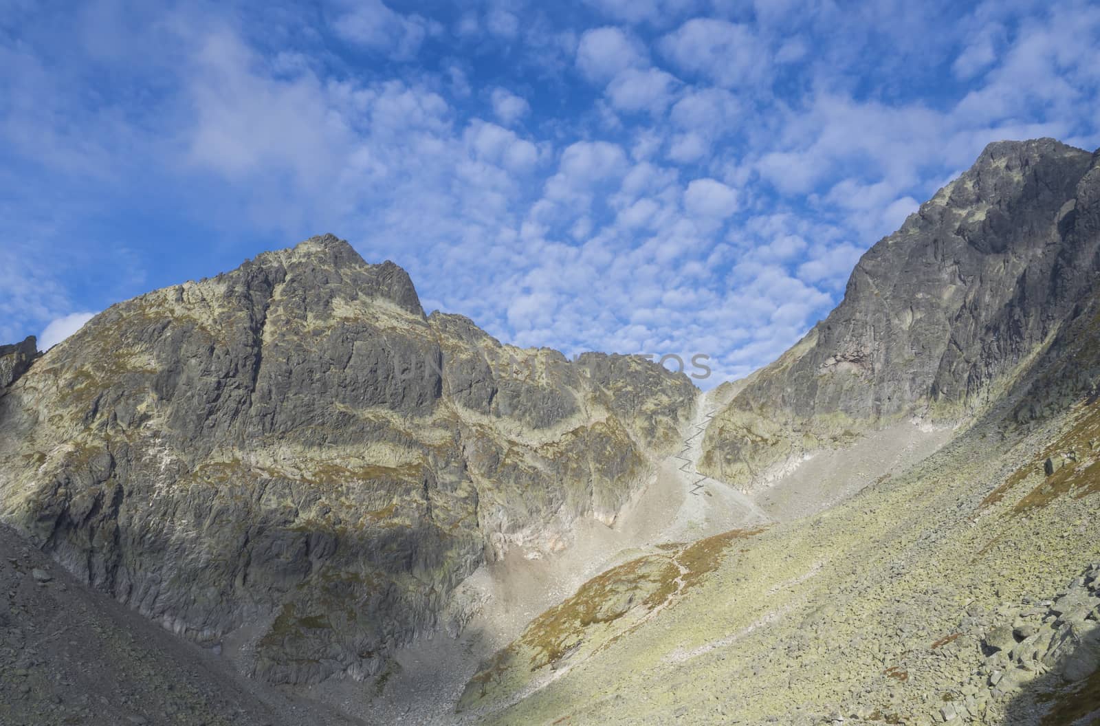 view on Sedielko mountain pass at 2 376 m with zig zag path on hiking route from the Teryho Chata mountain shelter to Tatranska javorina in the High Tatras in Slovakia, blue sky, white clouds.